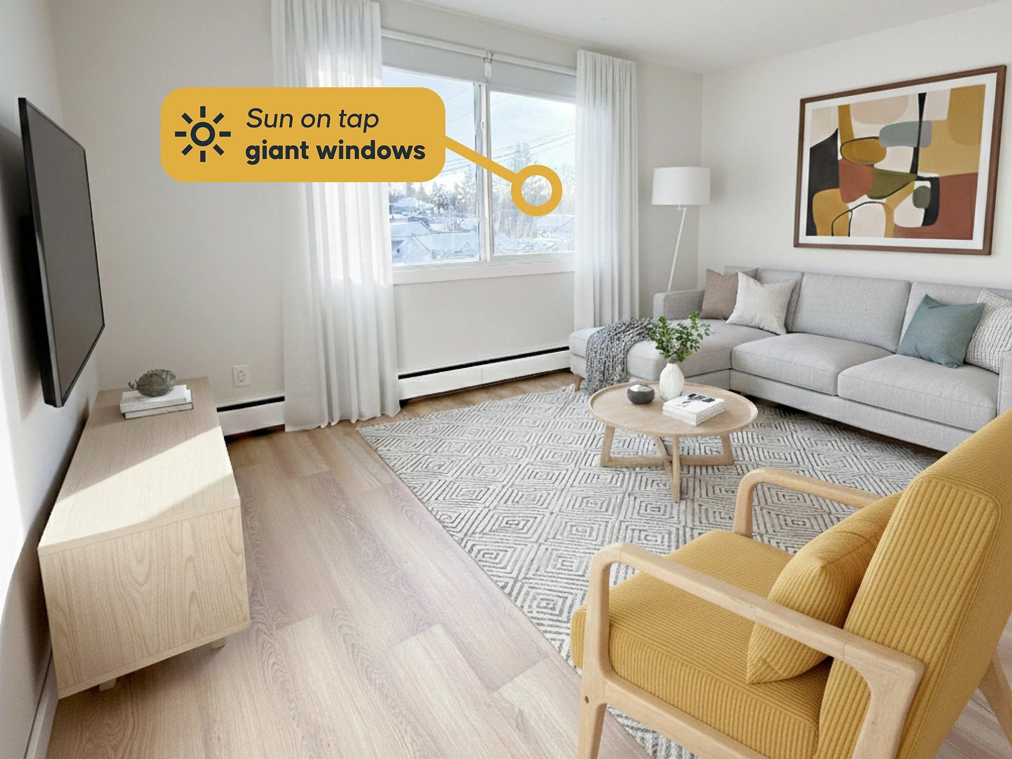 Living room with large windows, a white sectional sofa with pillows, a yellow armchair, a round wooden coffee table, a TV mounted on the wall, and abstract artwork on the wall. Sunlight streams through the giant windows.