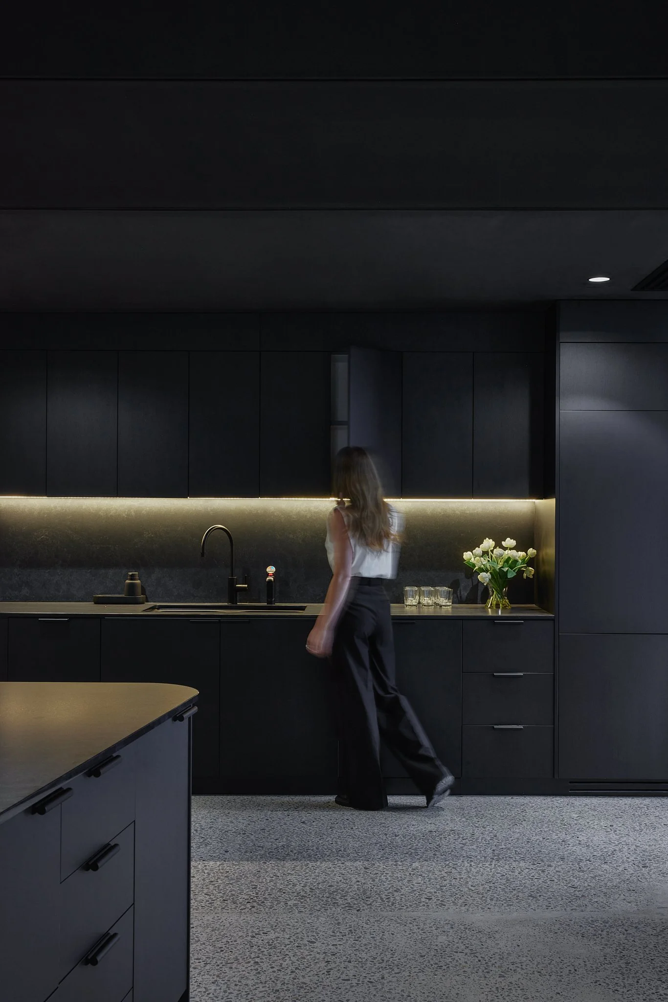 A woman opens a cupboard within a very moody kitchen painted in a very dark palette
