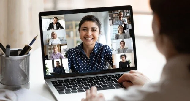 Person participating in a virtual video call on a laptop with multiple people, including a woman smiling.