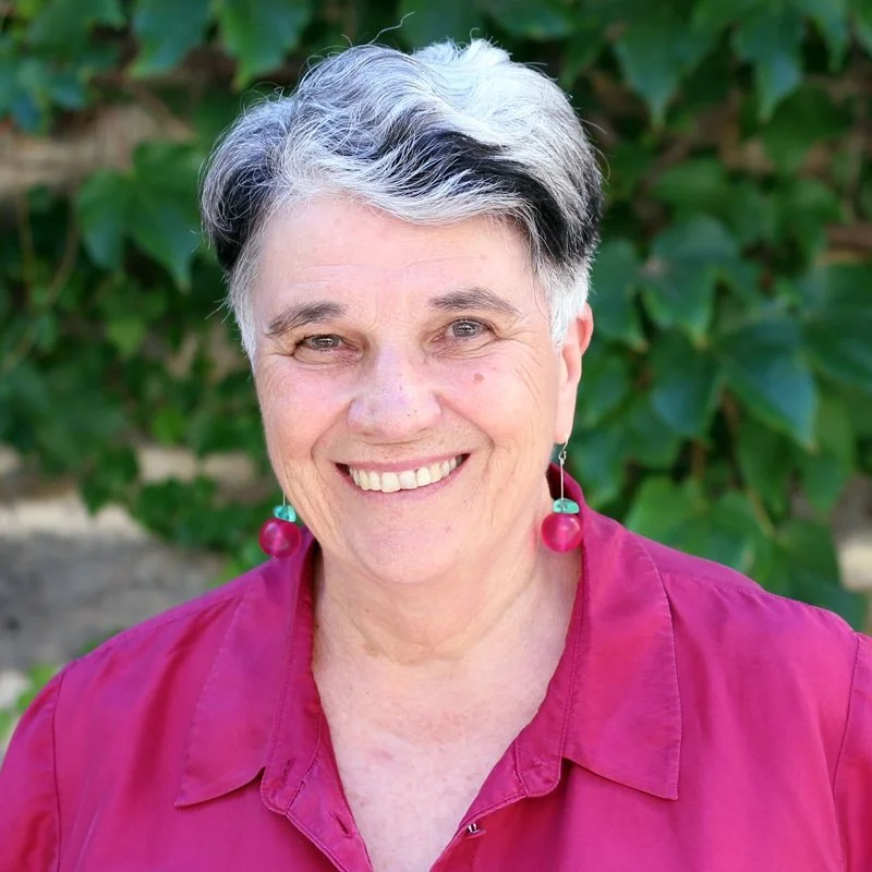 A photo of Dr Josie McLean, smiling and wearing a cherry coloured blouse and cherry earings - meaningful change