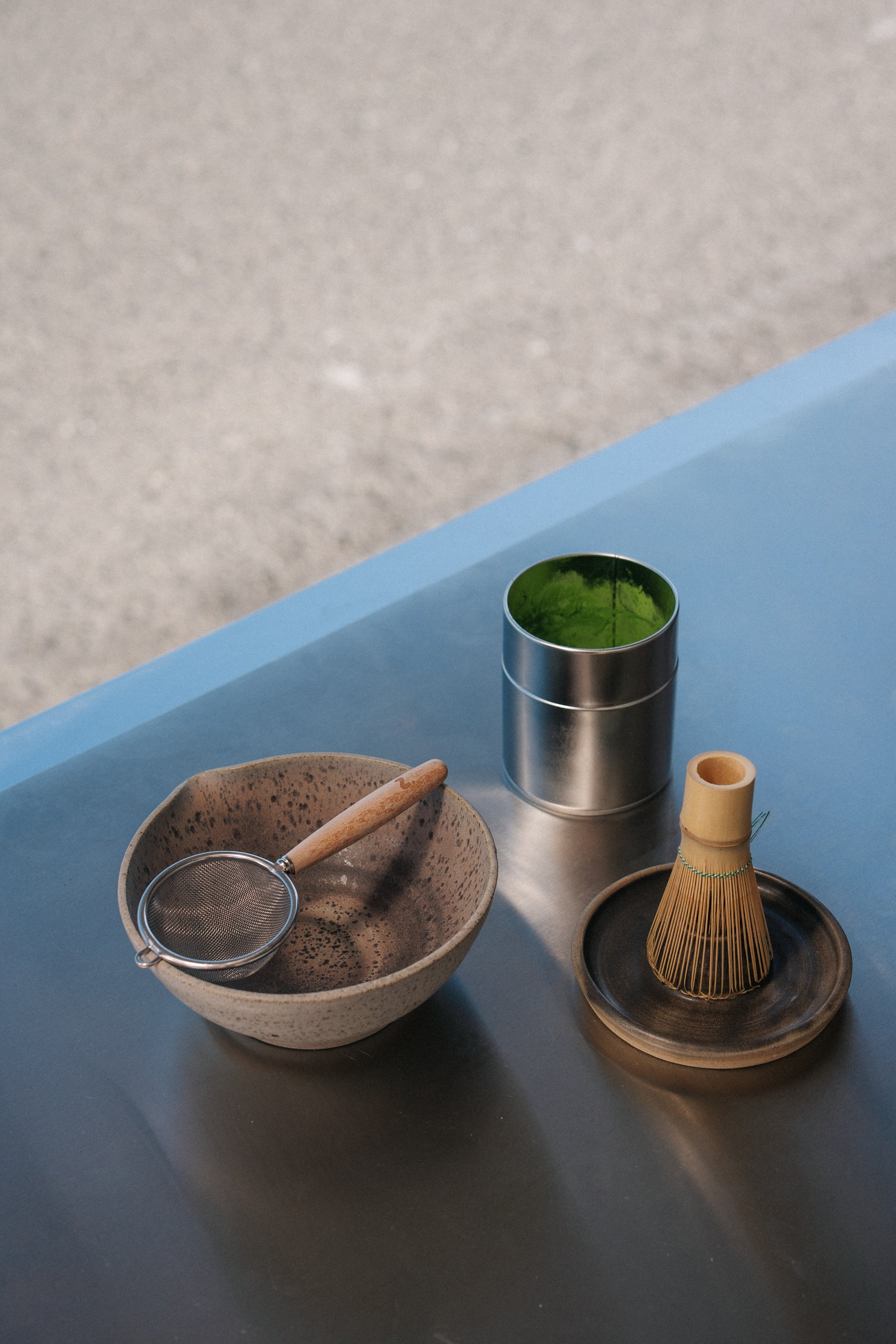 Matcha bowl with matcha sieve. Bamboo whisk situated on a ceramic matcha whisk holder. Matcha canister open with green matcha powder