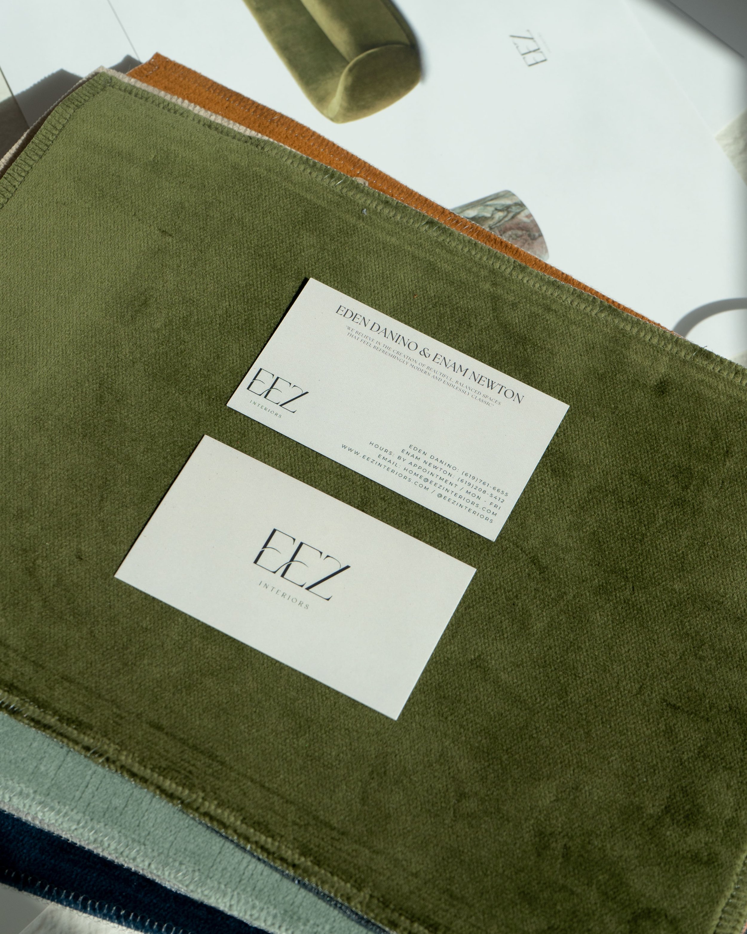 Swatches of fabric in various colors including green, with business cards from EEZ Interiors placed on top.