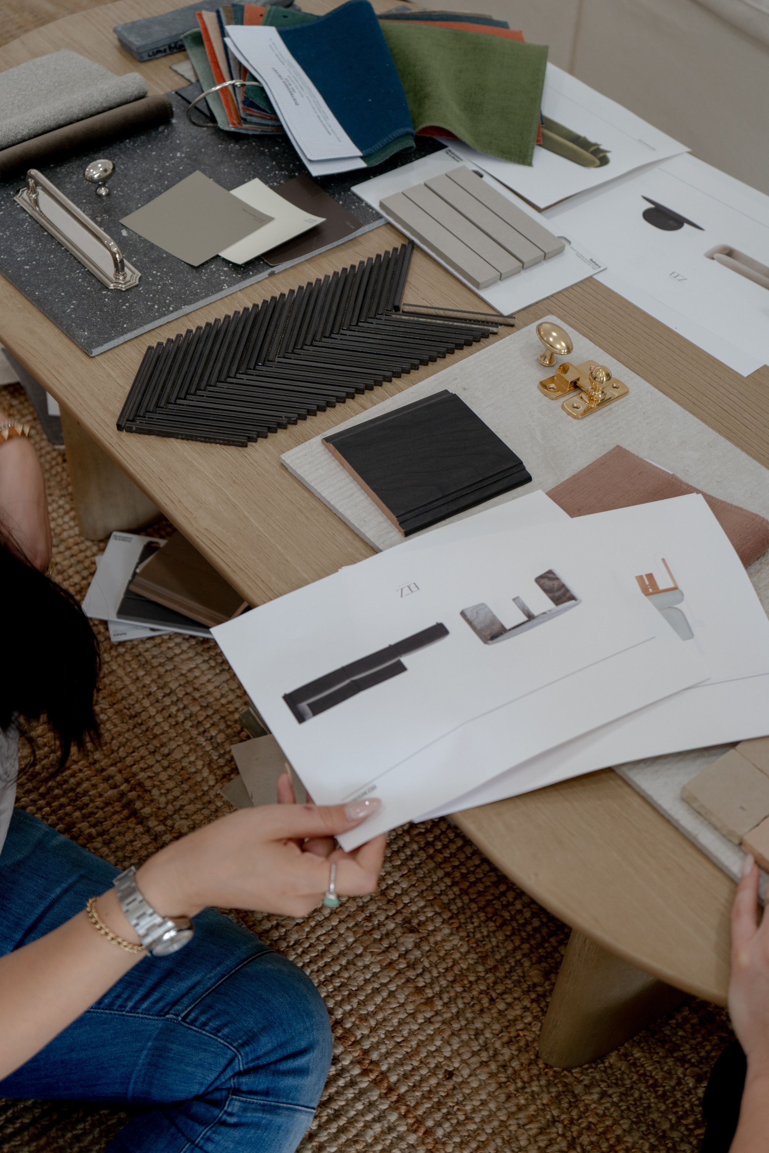 A table with various interior design materials including fabric swatches, color samples, tile designs, and metal hardware.