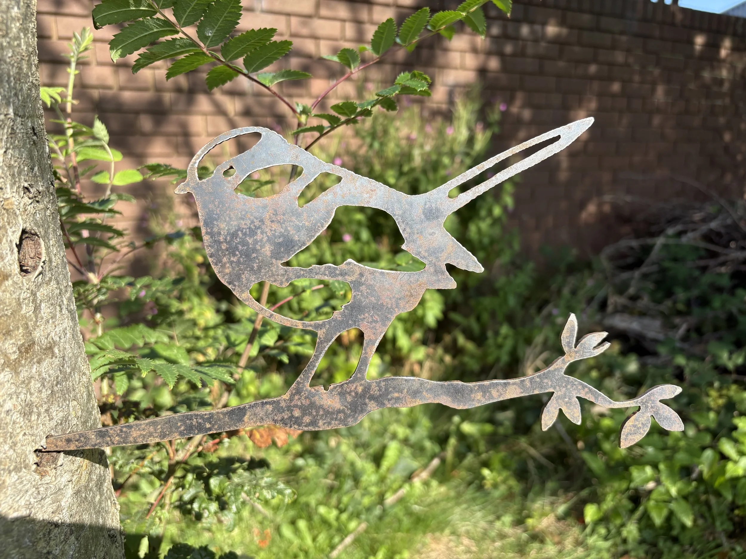 Metal blue tit silhouette perched on a twig, crafted from 3 mm mild steel with rust-ready finish—adds rustic charm to fences or borders.