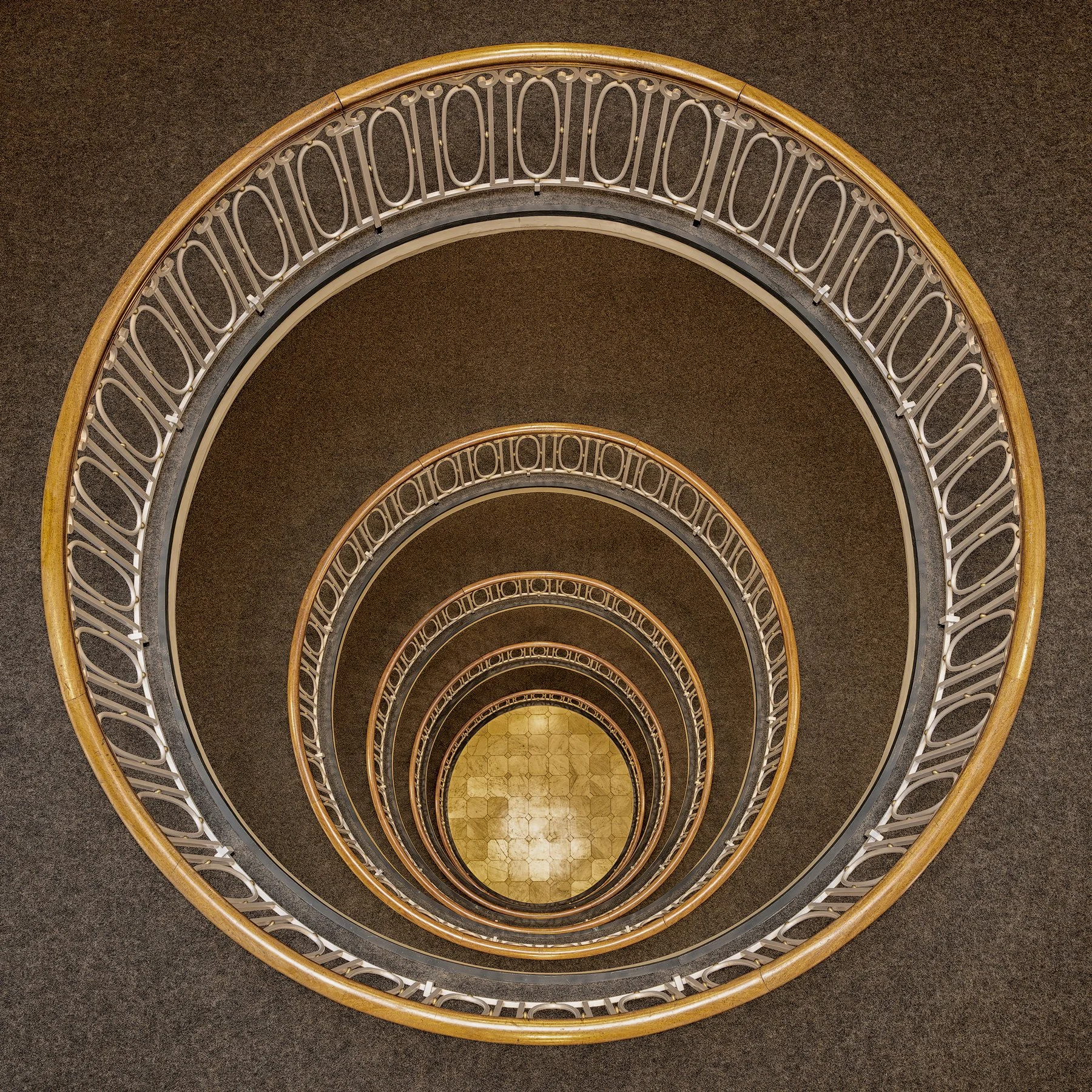 Historic interior architecture in Hamburg, Germany: A symmetrical bird’s-eye view of the elliptical spiral staircase within the Esplanadebau, designed by Distel & Grubitz. This architectural photograph captures the rhythmic descent of the concentric 