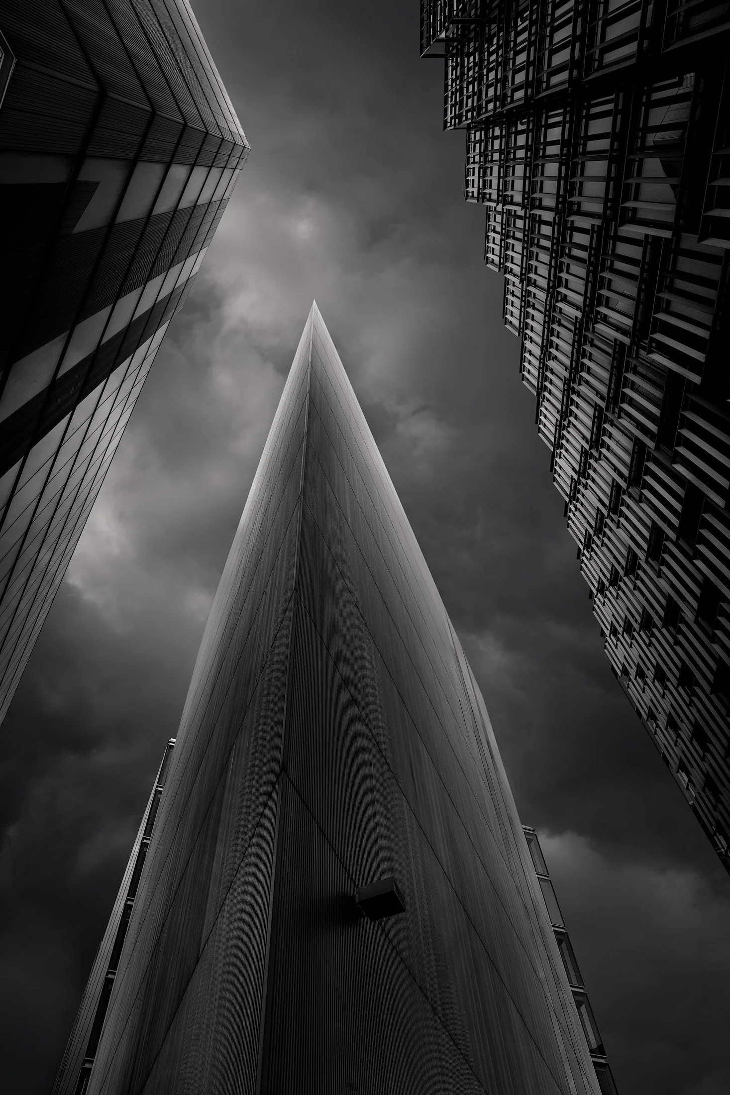 Contemporary urban geometry at More London: A dramatic monochromatic study of 7 More London Riverside, designed by Foster + Partners. This low-angle architectural photograph captures the building's sharp, prow-like silhouette as it pierces an atmosph
