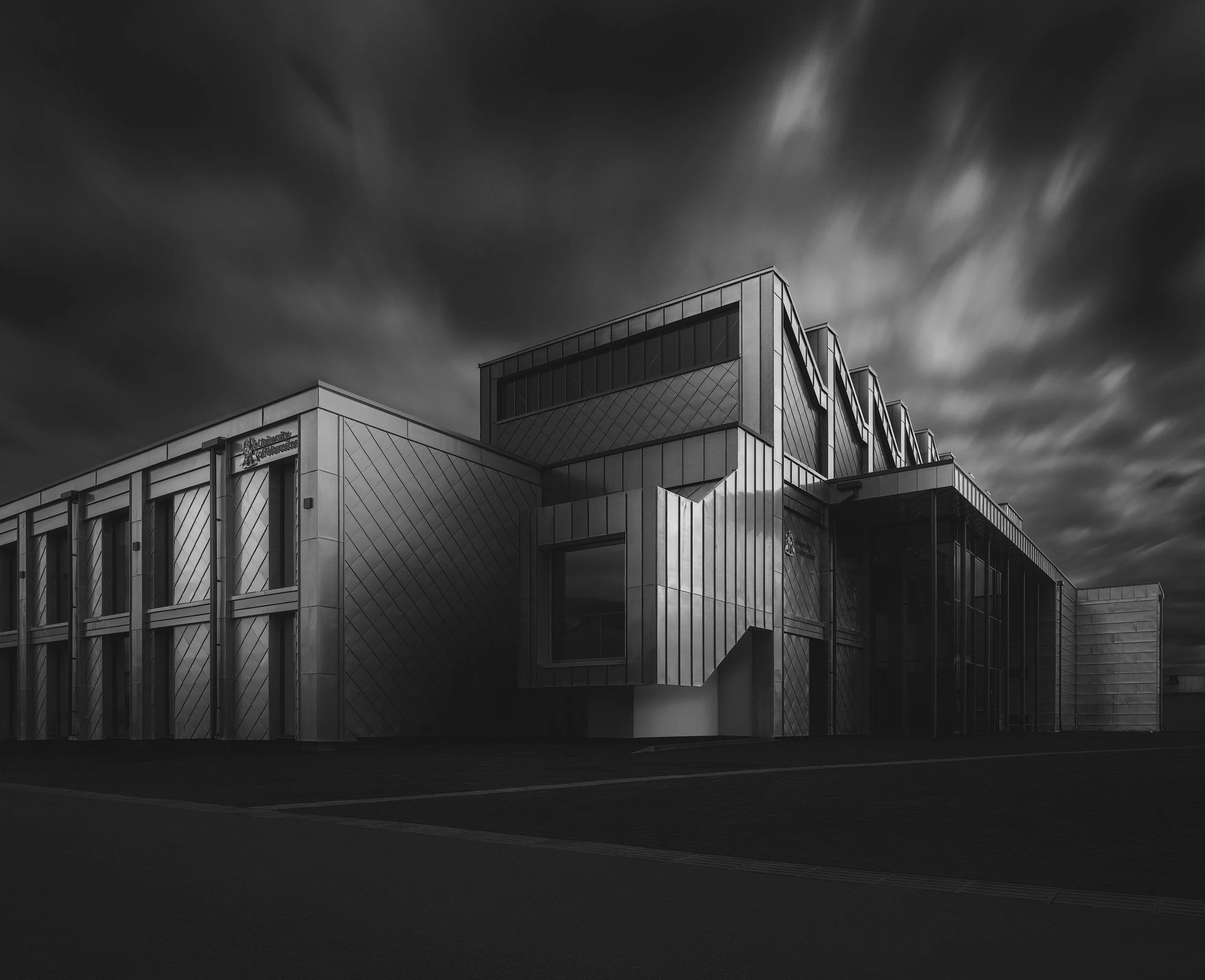 Sustainable educational architecture in Worcester, England: A dramatic long-exposure study of the Elizabeth Garrett Anderson Building, designed by BMJ Architects for the University of Worcester. This monochromatic photograph highlights the building’s
