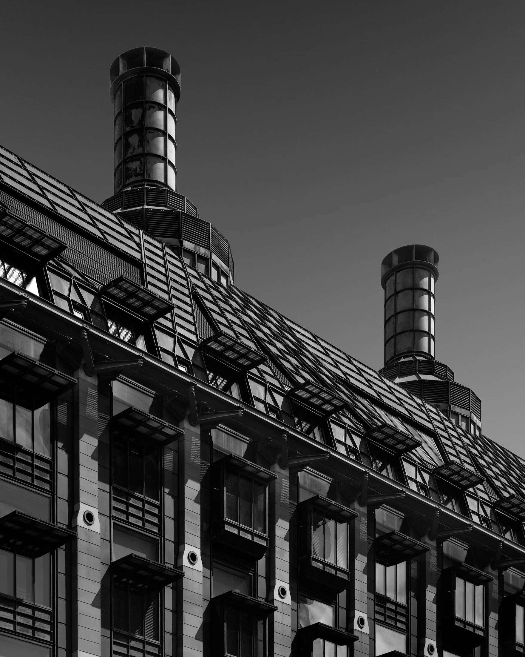 High-tech civic architecture in Westminster, London: A dramatic monochromatic study of Portcullis House, designed by Michael Hopkins and Partners. This vertical architectural photograph captures the building’s unique roofline, defined by its dark bro