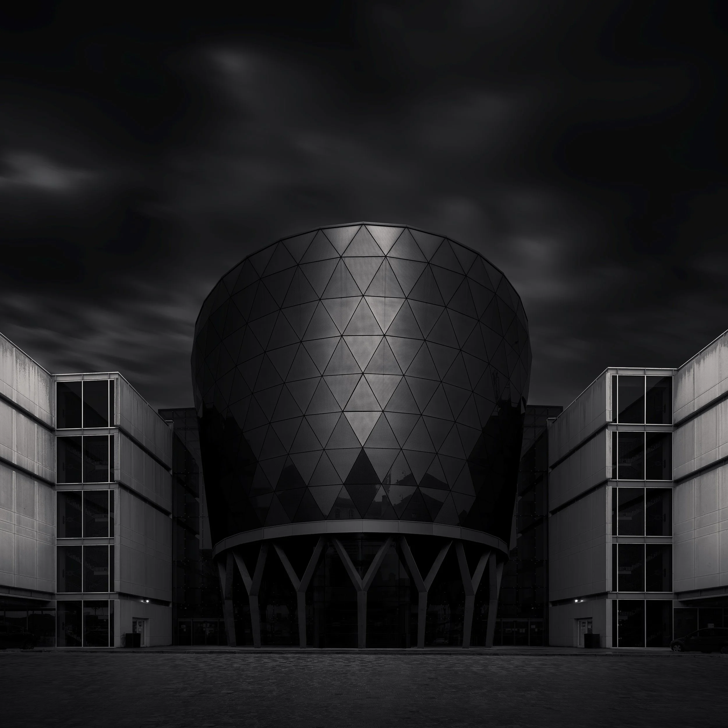 [architecture] [uk] [leeds] [blackandwhite] [square] Rose Bowl Leeds Beckett University, triangulated glazed drum elevated on branching columns, dramatic dark monochrome. Architectural Photography by Jim Scott.