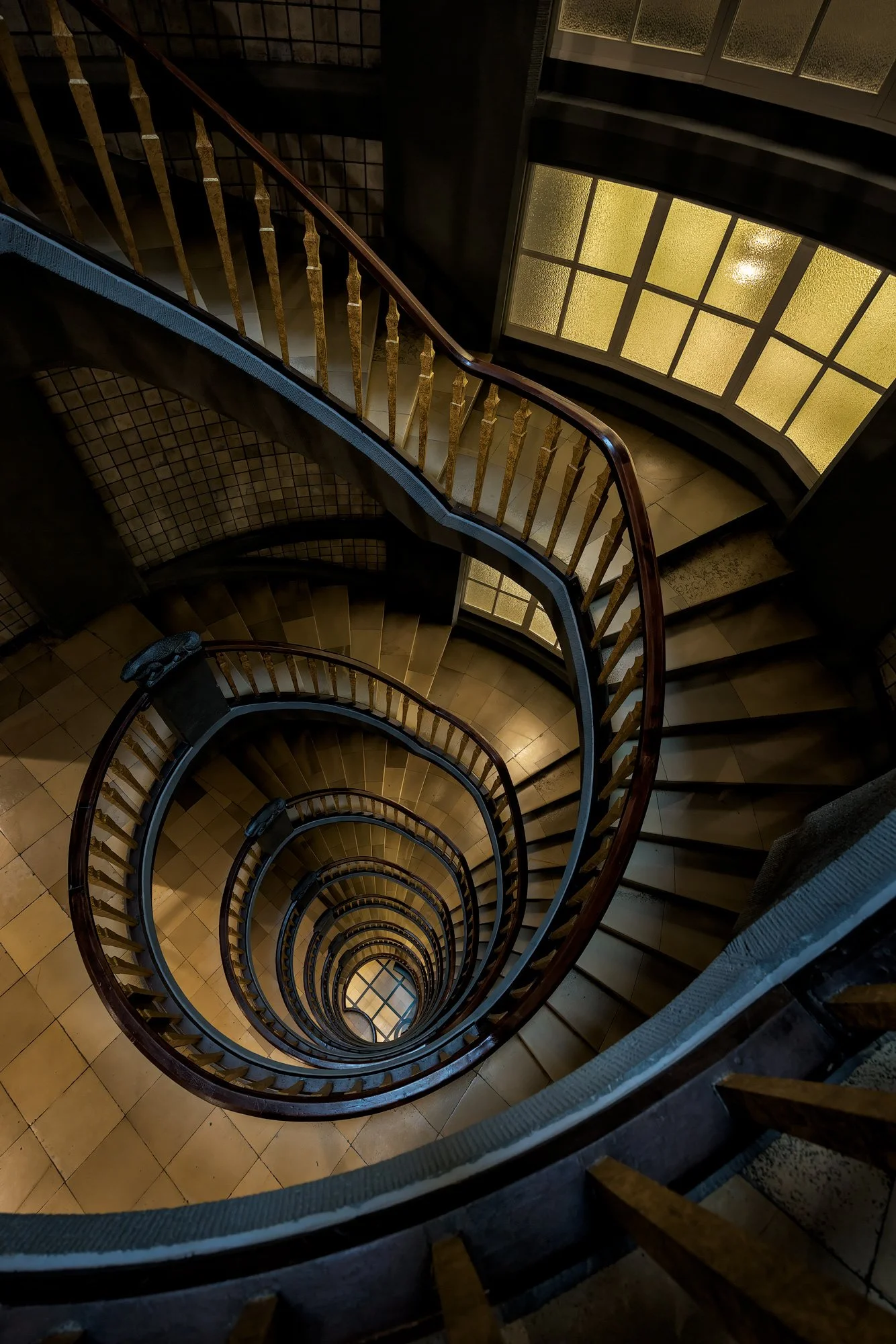 Brick Expressionist interior in Hamburg, Germany: A mesmerising study of the spiral staircase within the Meßberghof, a UNESCO World Heritage site. This high-angle architectural photograph captures the rhythmic, concentric geometry of the wooden handr