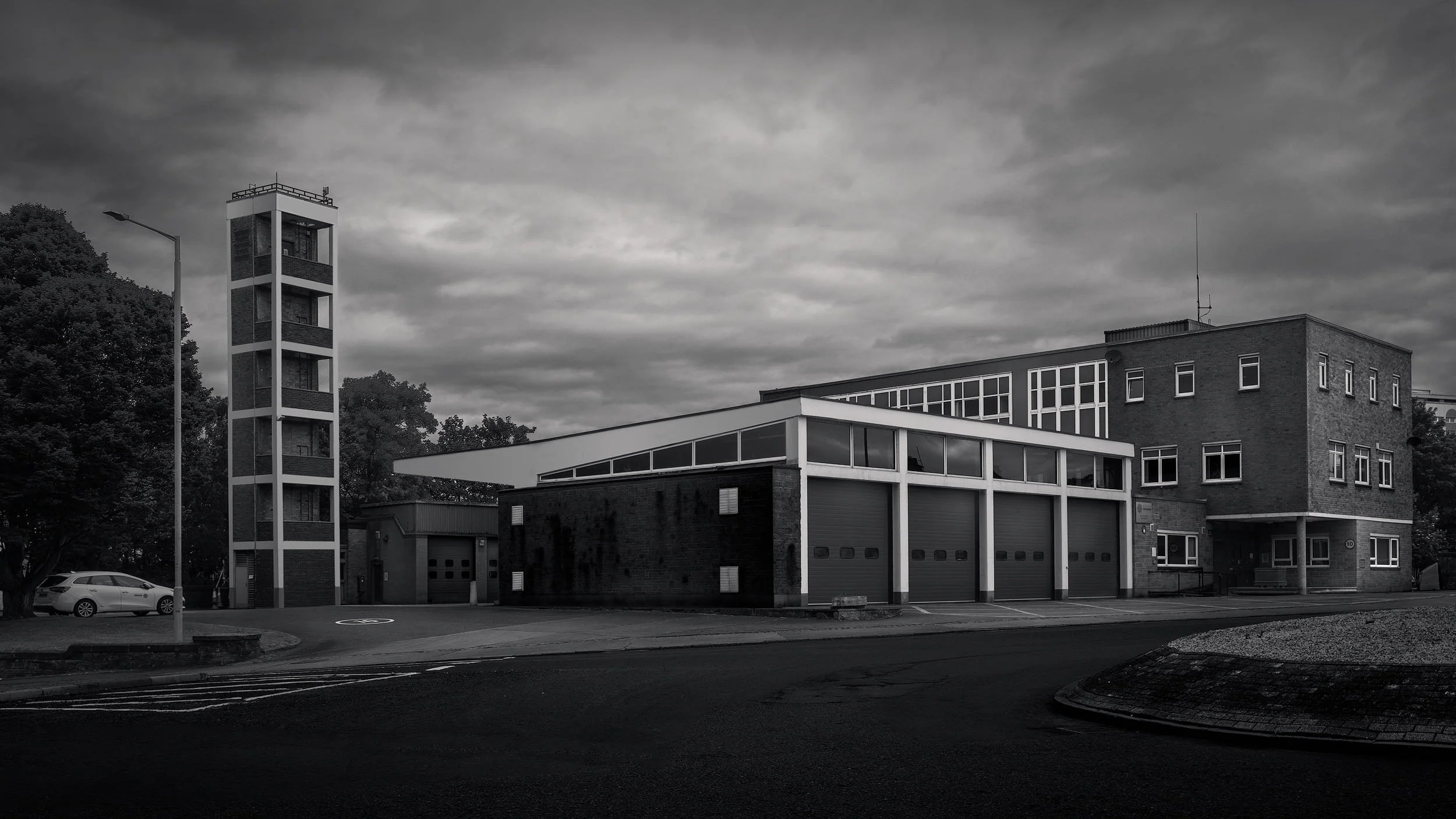 [architecture] [uk] [ayr] [blackandwhite] Ayr Fire Station monochrome, modernist brick facade, practice drill and flat canopy under a dramatic long exposure sky. Architectural Photography by Jim Scott.