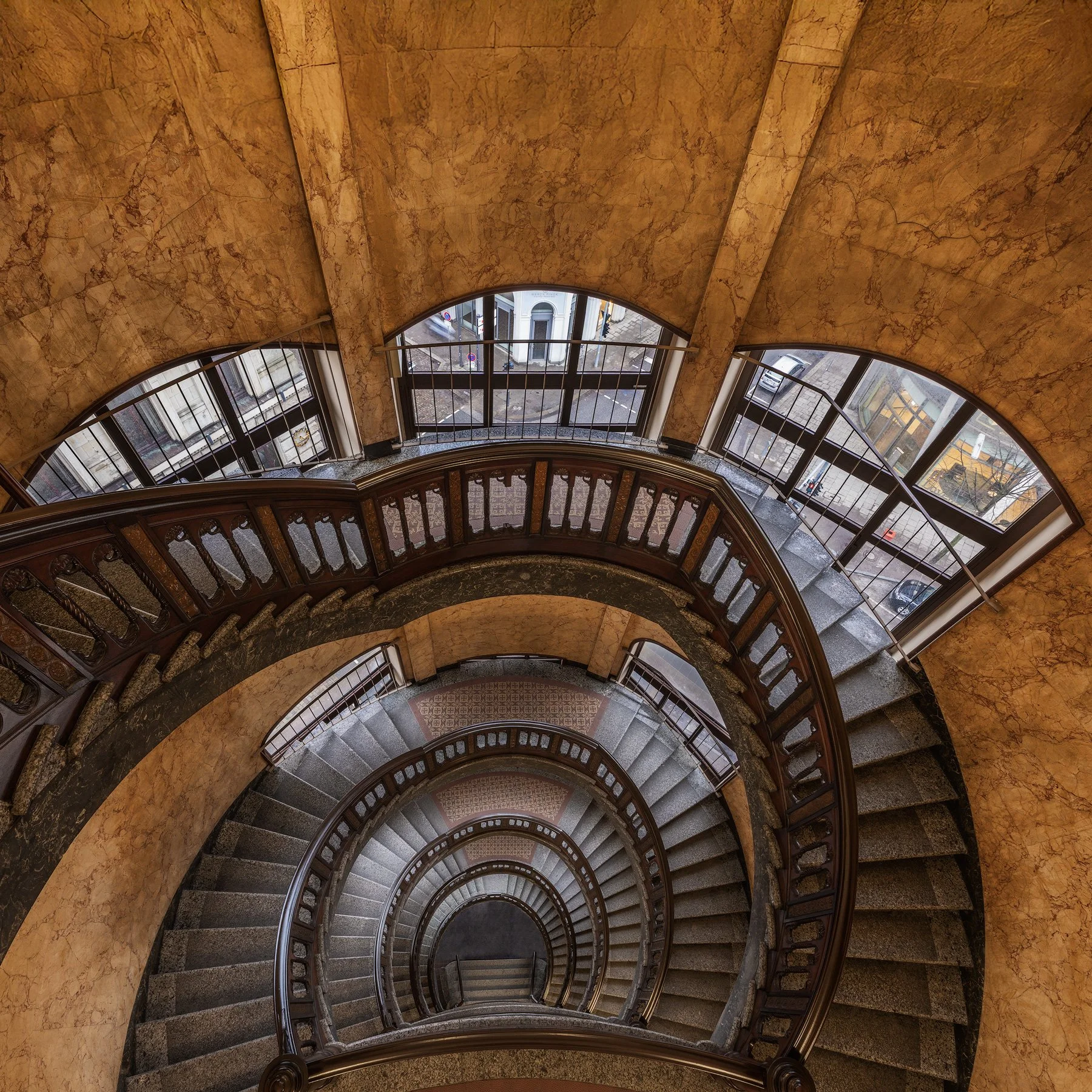 Historic interior architecture in Hamburg, Germany: A captivating wide-angle study of the spiral staircase within the Alstertor office building. This top-down architectural photograph captures the rhythmic, descending curves of the stone steps and th