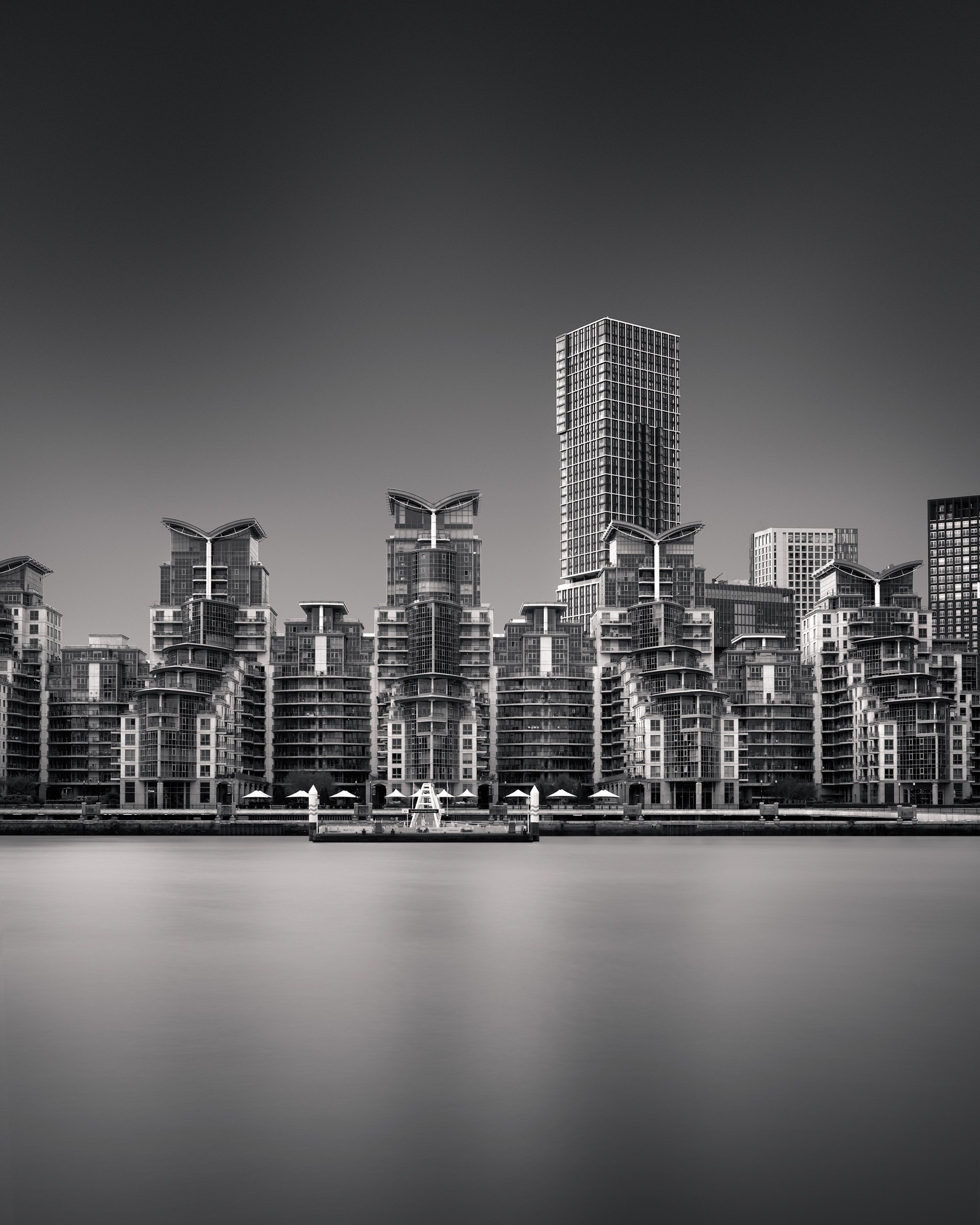 Contemporary riverside architecture in Vauxhall, London: A dramatic monochromatic study of St George Wharf and the Vauxhall Tower, designed by Broadway Malyan. This long-exposure photograph captures the development’s iconic gull-wing roofs and rhythm
