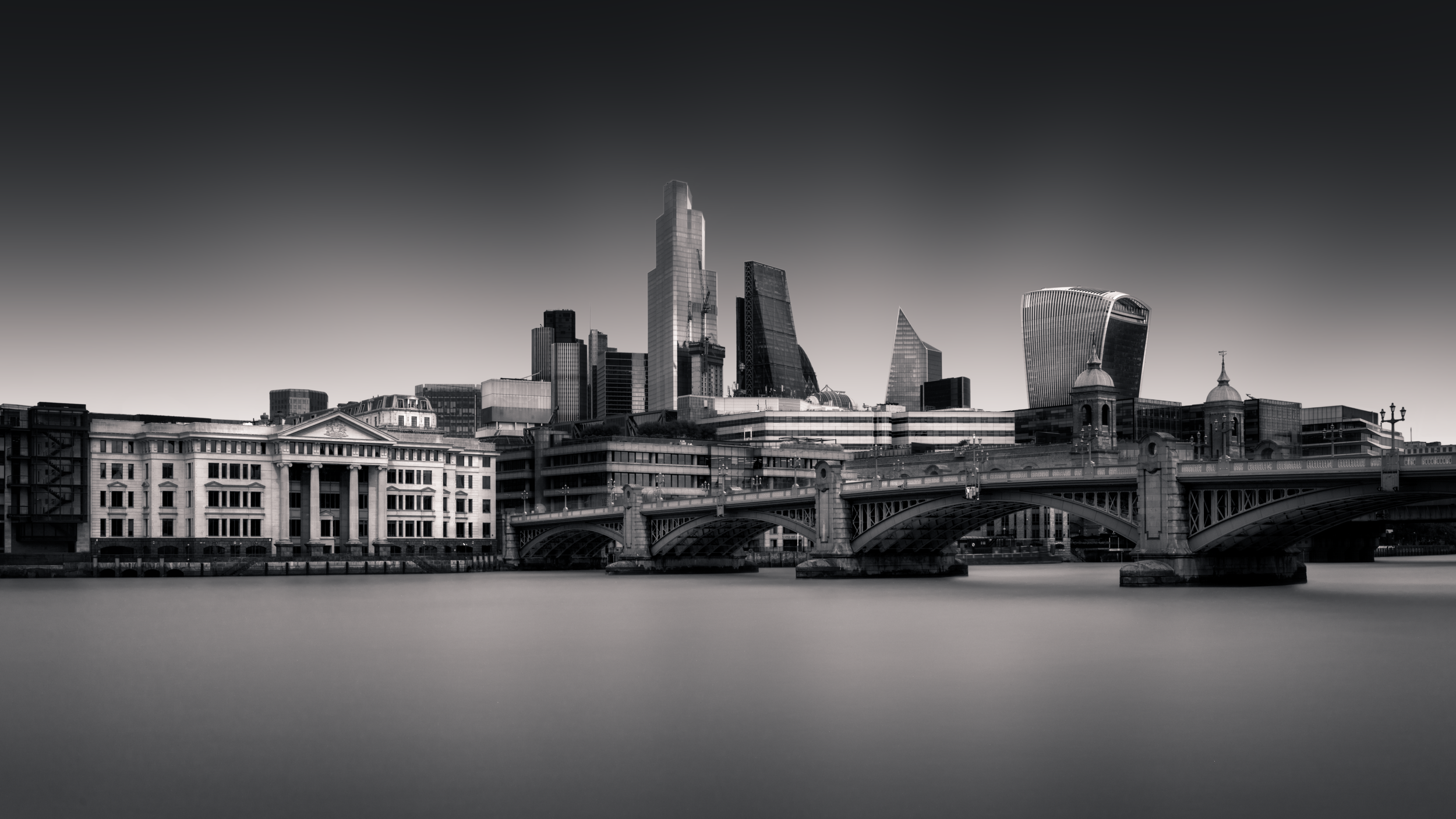 Long exposure black and white photograph of the City of London skyline from Bankside Pier, featuring Southwark Bridge and the financial district skyscrapers including 22 Bishopsgate and the Walkie-Talkie