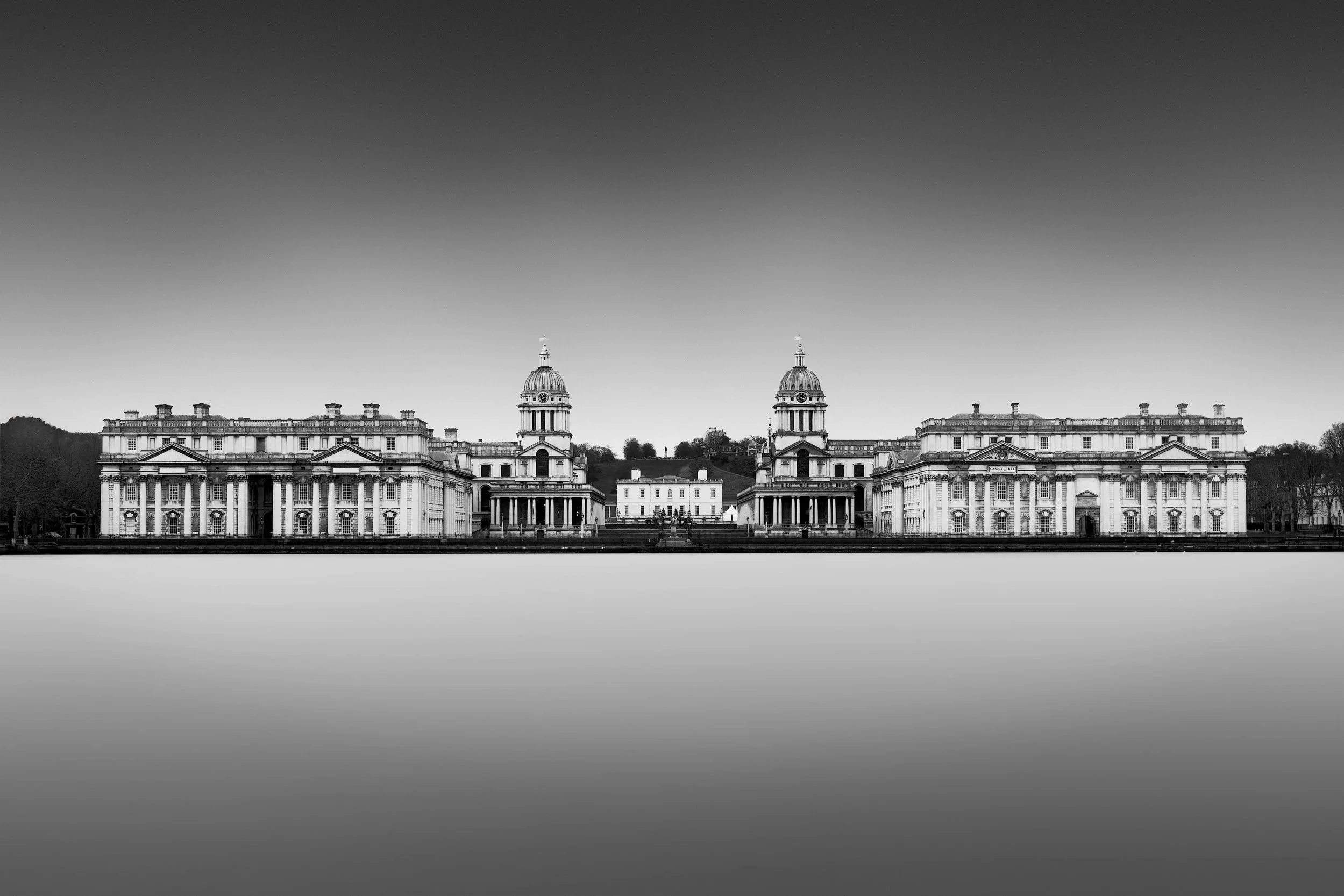 [architecture] [uk] [london] [blackandwhite] [panoramic] Old Royal Naval College Greenwich B&W, full symmetrical Baroque facade with twin domes above a silken smooth Thames. Architectural Photography by Jim Scott.