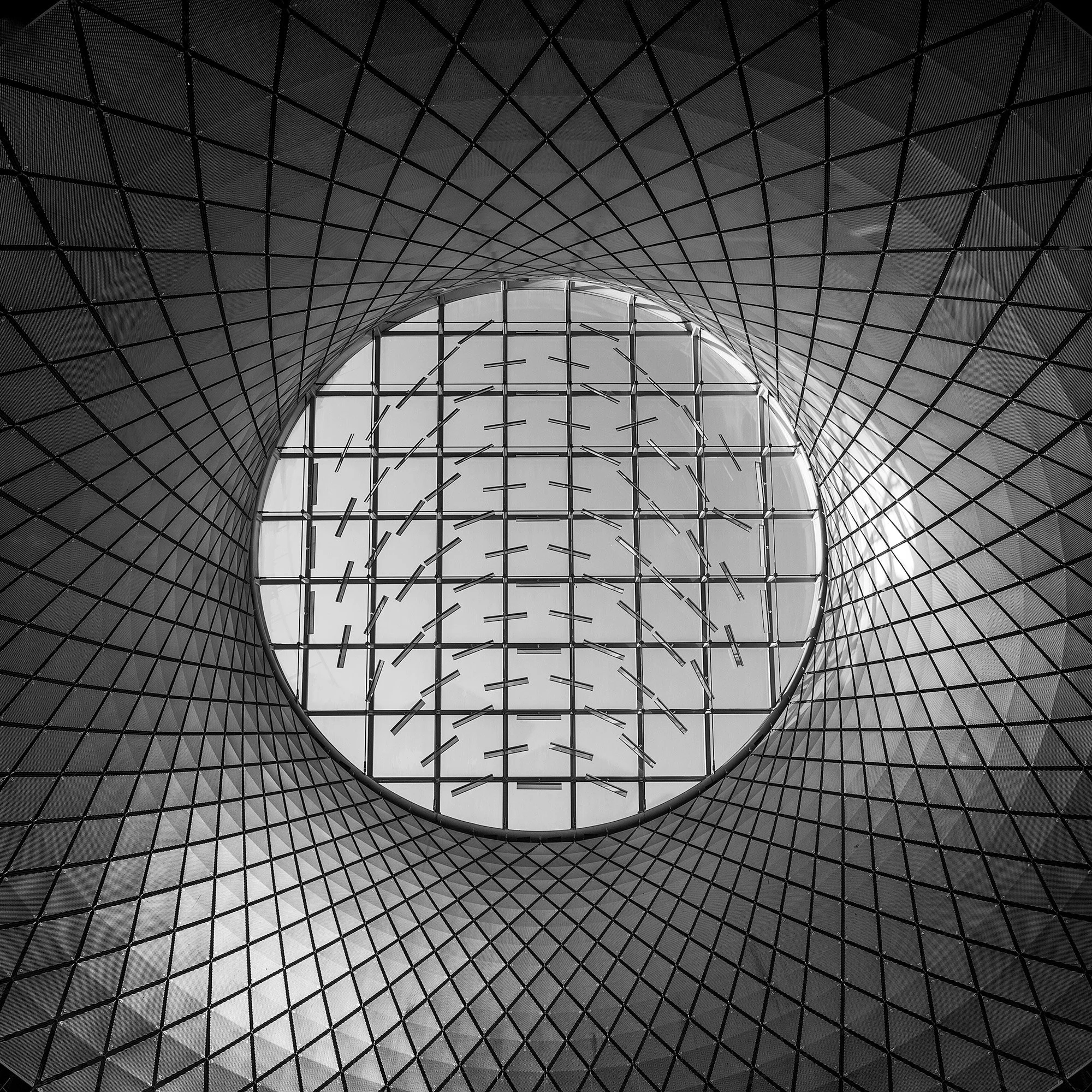 High-tech transit architecture in New York City: A symmetrical monochromatic study of the Sky Reflector-Net at the Fulton Center, designed by Grimshaw Architects. This architectural photograph captures the upward-looking "oculus" and its intricate ca