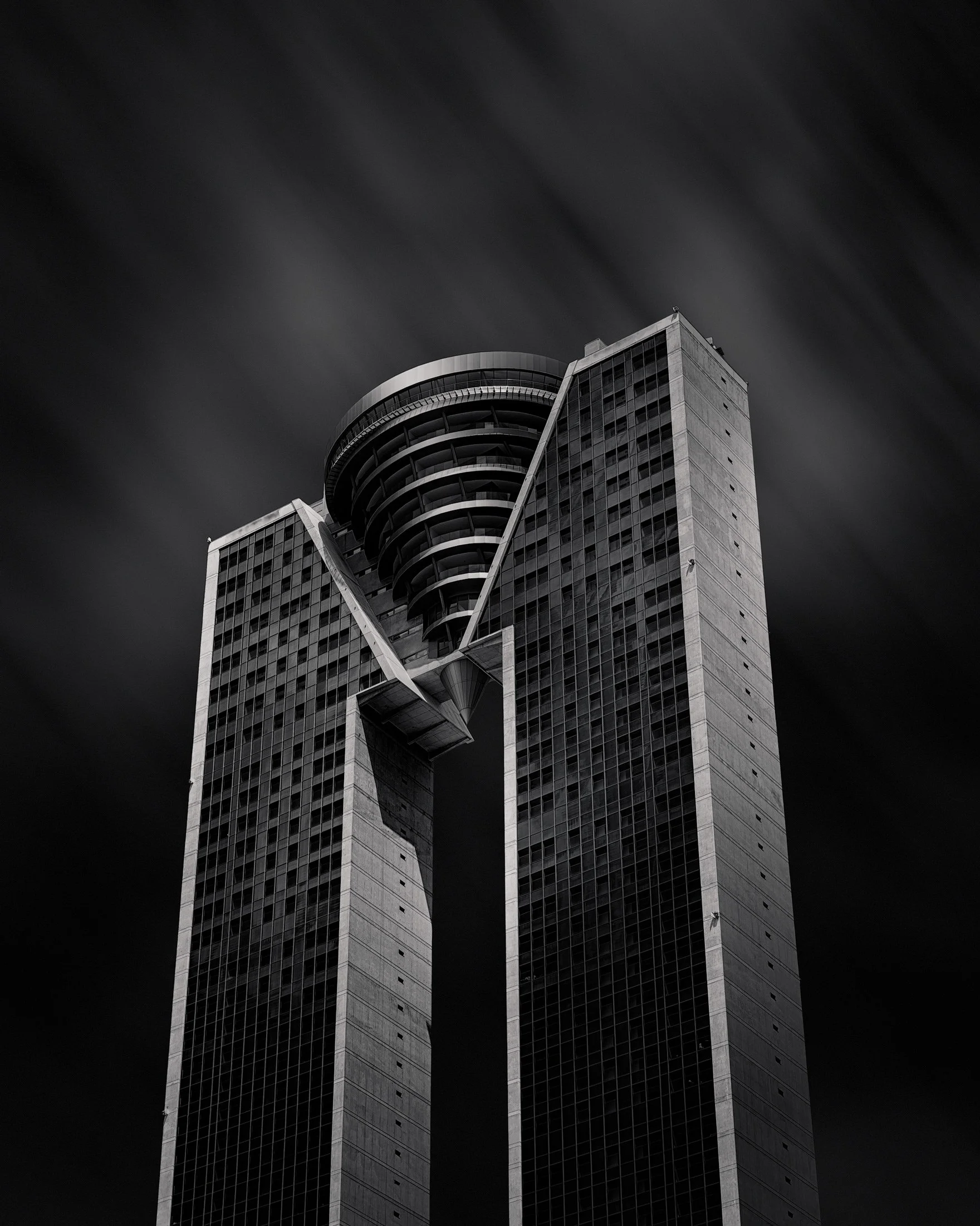 [architecture] [europe] [benidorm] [ blackandwhite] Intempo Tower Benidorm monochrome, twin concrete slabs bridged by a circular crown dissolving into a streaked sky. Architectural Photography by Jim Scott.