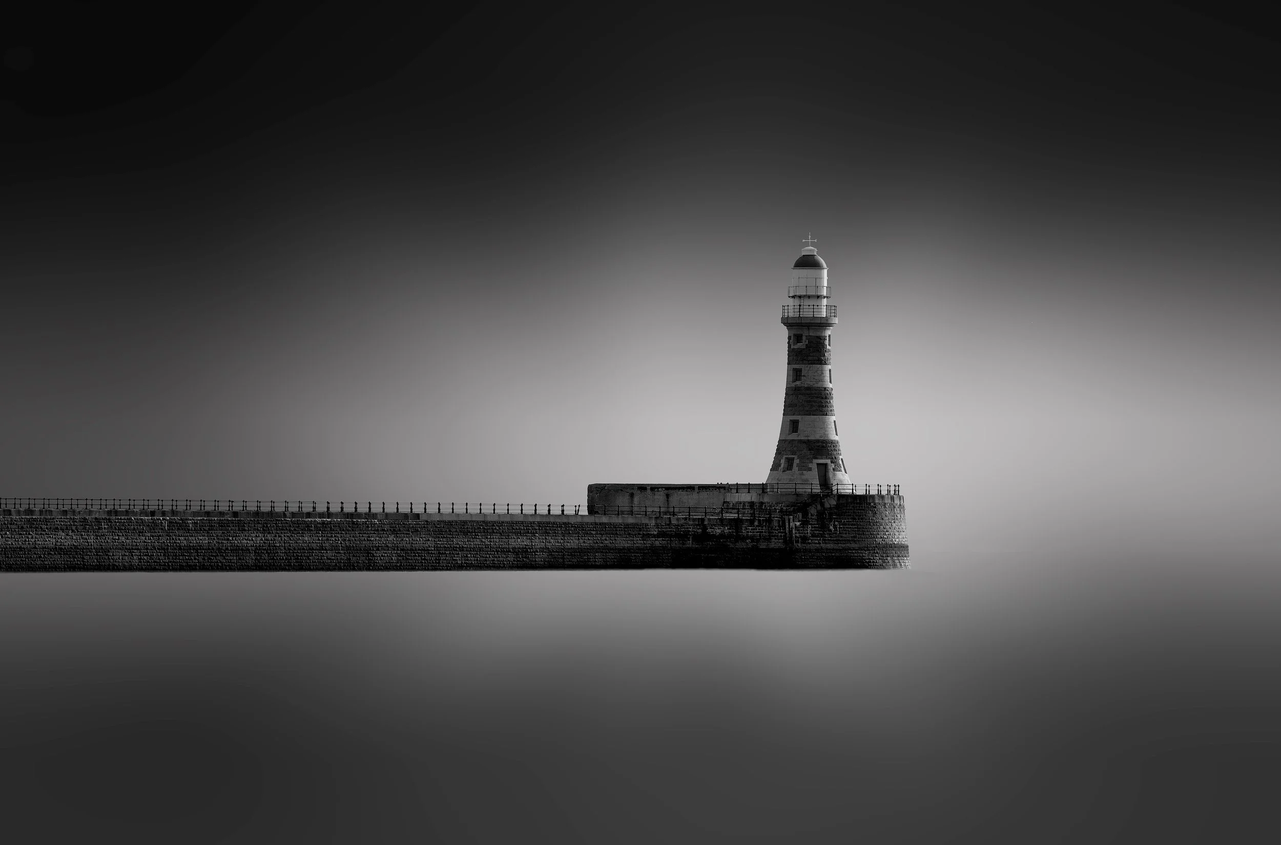 Victorian marine engineering in Sunderland, UK: A minimalist monochromatic study of Roker Pier and Lighthouse, designed by Henry Hay Wake. This long-exposure photograph captures the iconic banded tower and granite pier isolated against a seamless, et