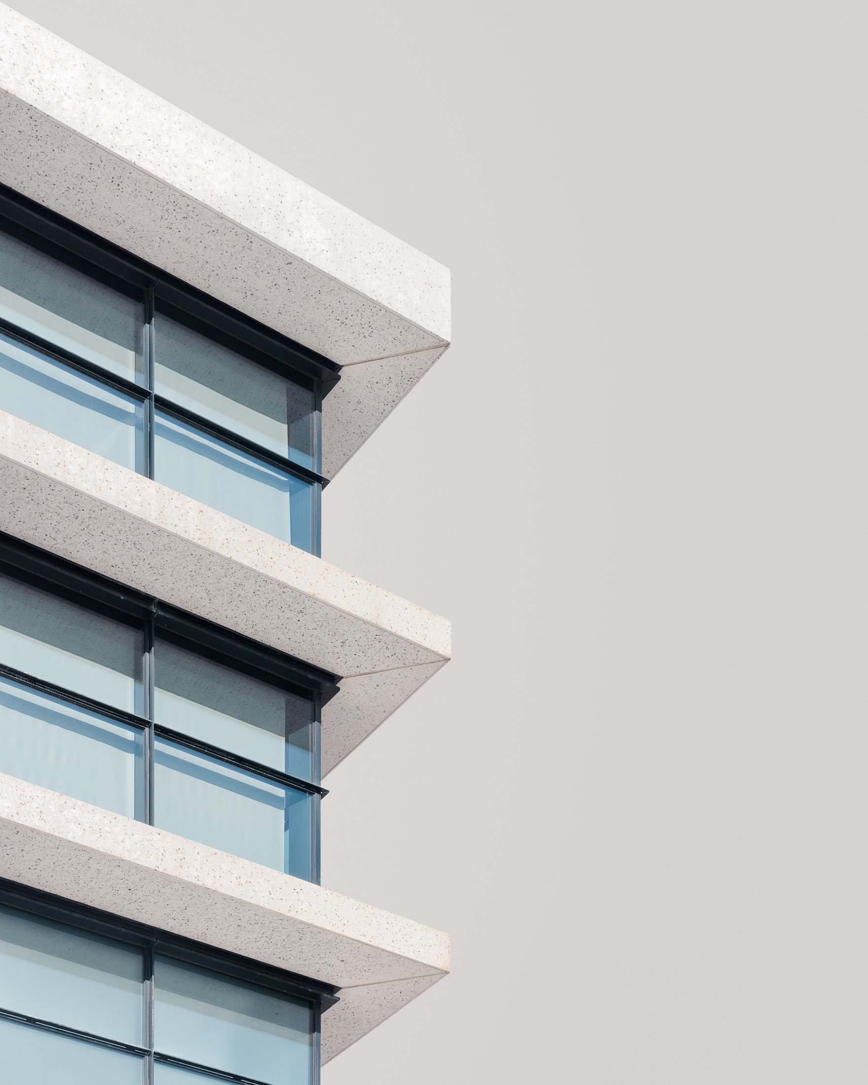 Contemporary residential architecture at Lewis Cubitt Square, King's Cross, London. A minimalist architectural photograph featuring a detail of the building’s facade, highlighting the geometric rhythm of the protruding stone balconies and sleek glass