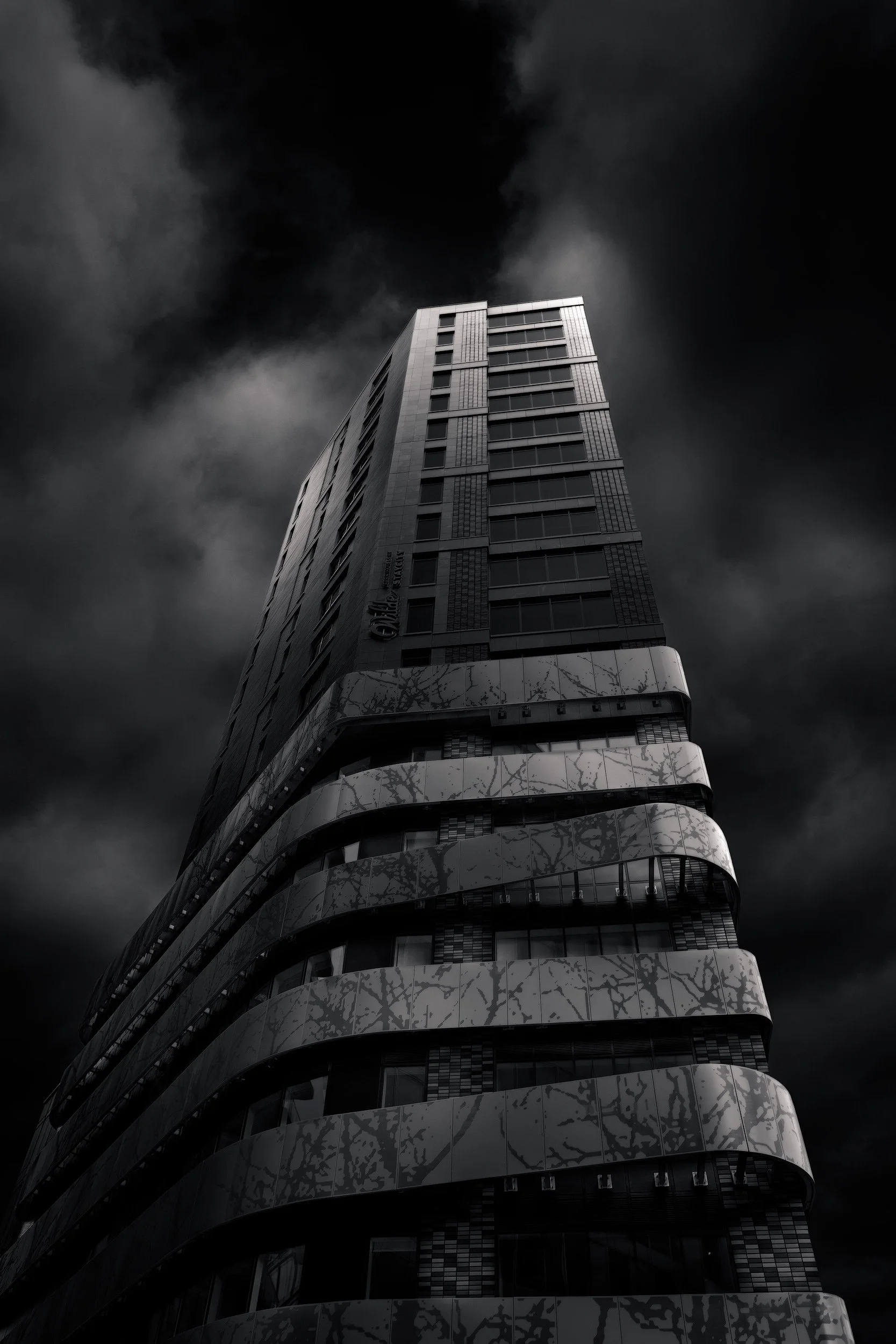 [architecture] [uk] [london] [blackandwhite] Wilde Aparthotel Paddington London, soaring tower with blossom-printed curved balcony bands, low angle dramatic black and white. Architectural Photography by Jim Scott.