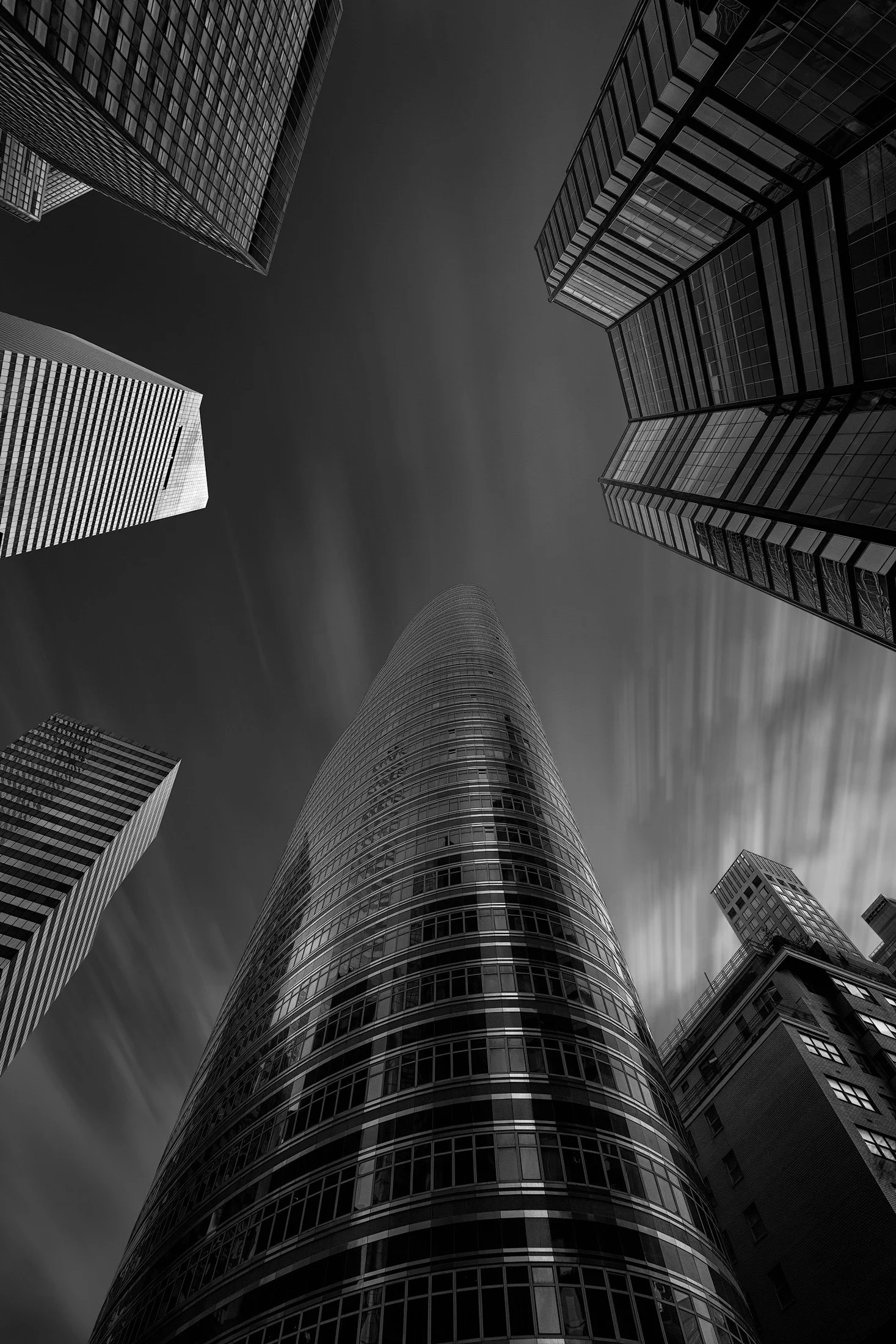 Postmodern skyscraper architecture in Manhattan, NYC: A dramatic monochromatic "worm's-eye" study of the Lipstick Building, designed by Philip Johnson and John Burgee. This low-angle photograph captures the building’s unique elliptical tiers framed b