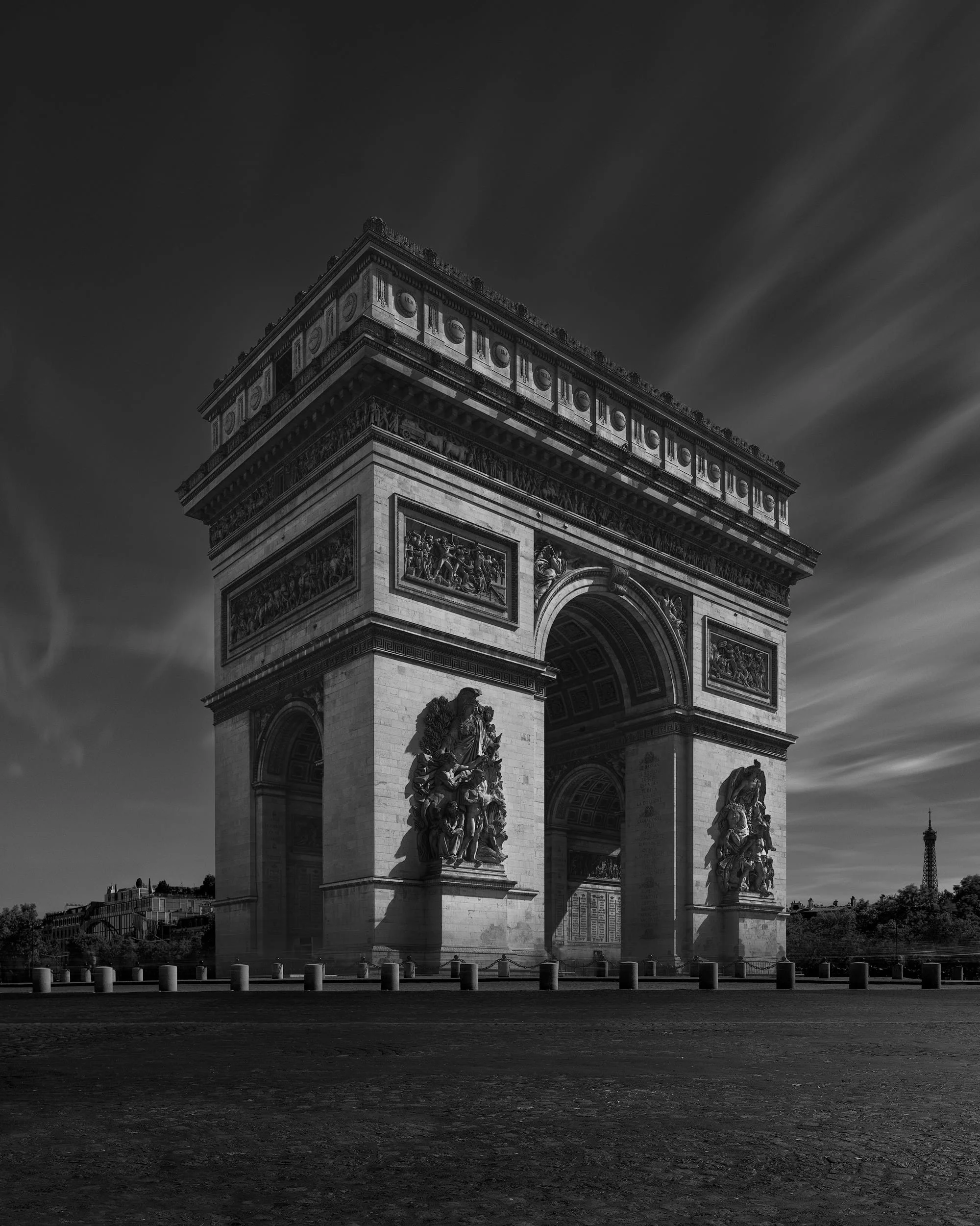 [architecture] [europe] [paris] [blackandwhite] Arc de Triomphe Paris B&W long exposure, relief sculptures in sharp detail, Eiffel Tower silhouetted in the distance. Architectural Photography by Jim Scott.