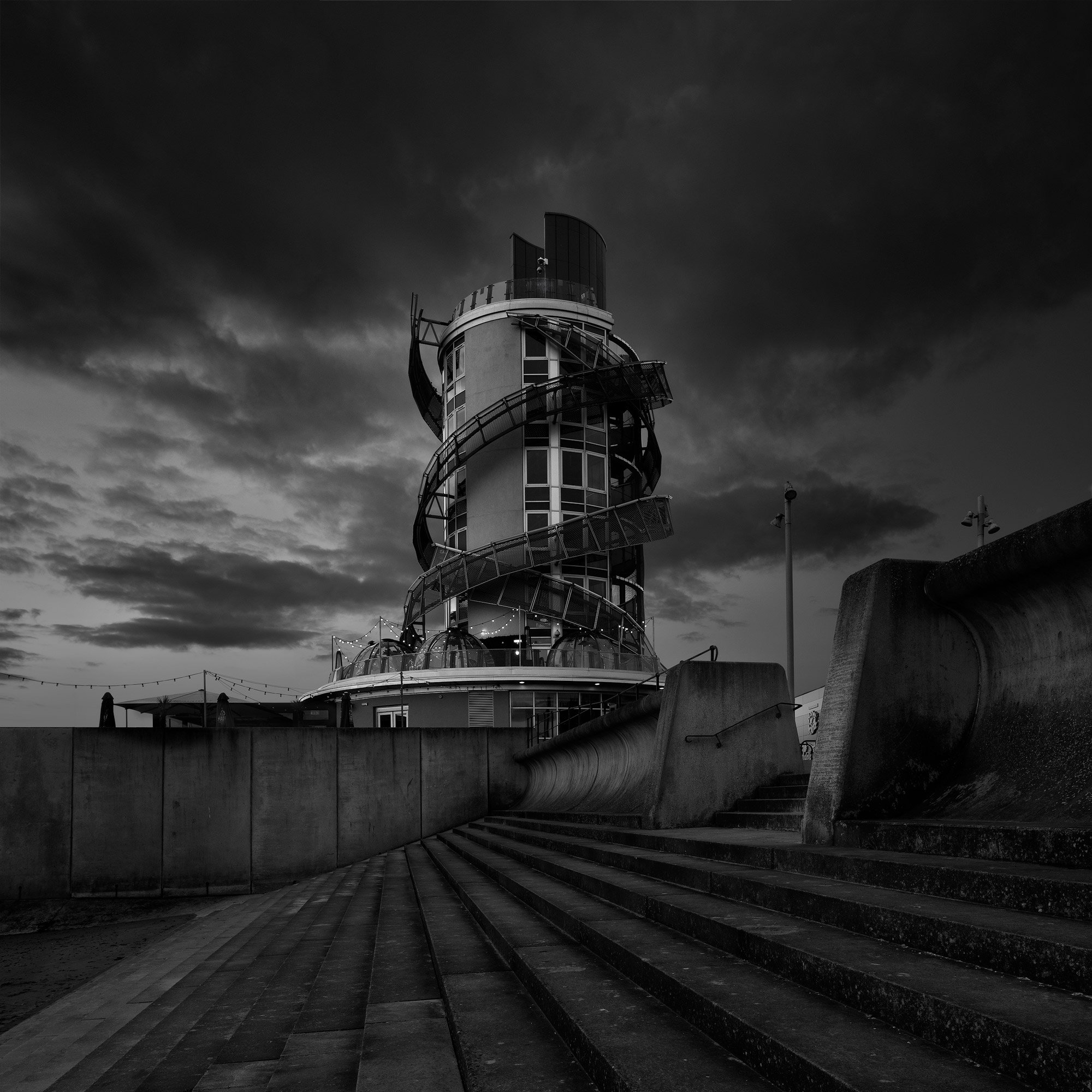 [architecture] [uk] [redcar] [blackandwhite] [square] Redcar Beacon, cylindrical glazed observation tower with helical external staircase rising from concrete steps. Architectural Photography by Jim Scott.