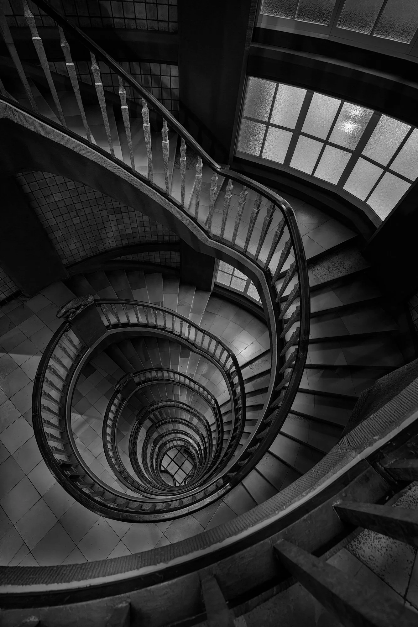 Historic Expressionist architecture in Hamburg, Germany: A dramatic monochromatic study of the spiral staircase within the Meßberghof, designed by Hans and Oskar Gerson. This top-down architectural photograph captures the dizzying, rhythmic descent o