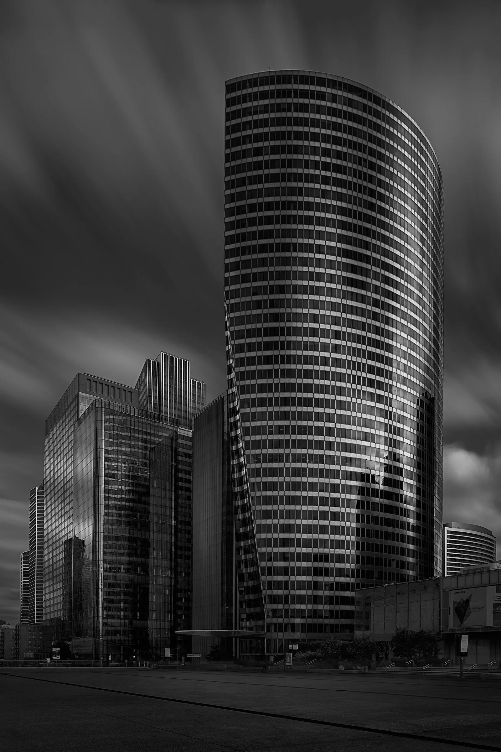 [architecture] [europe] [paris] [blackandwhite] Tour La Défense Paris B&W long exposure, dominant curved glass cylinder tower rising above surrounding slab towers. Architectural Photography by Jim Scott.