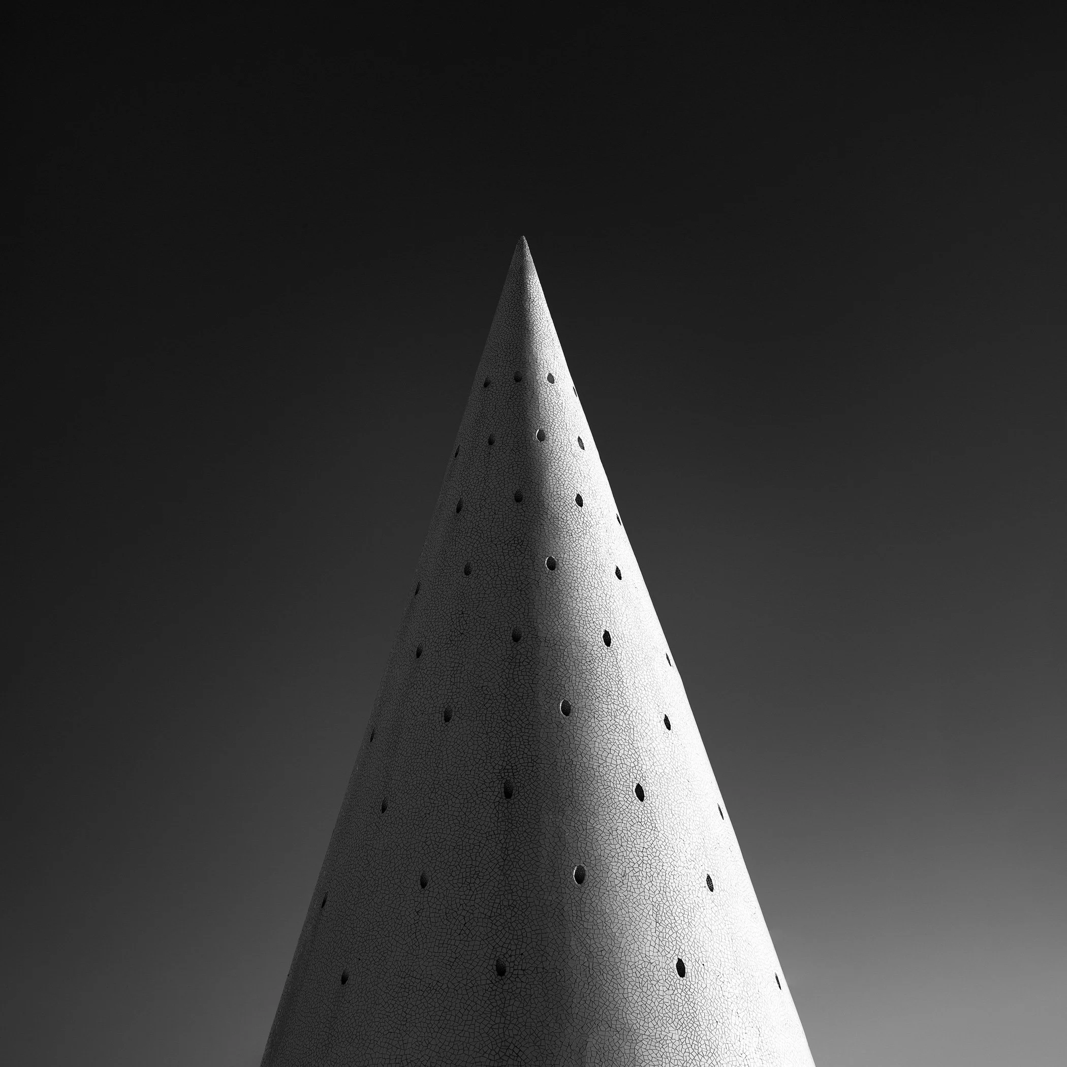 Minimalist architectural abstract in Valencia, Spain: A study of a sculptural ventilation pylon at the City of Arts and Sciences, designed by Santiago Calatrava. This high-contrast black and white photograph emphasizes the conical geometry and the in