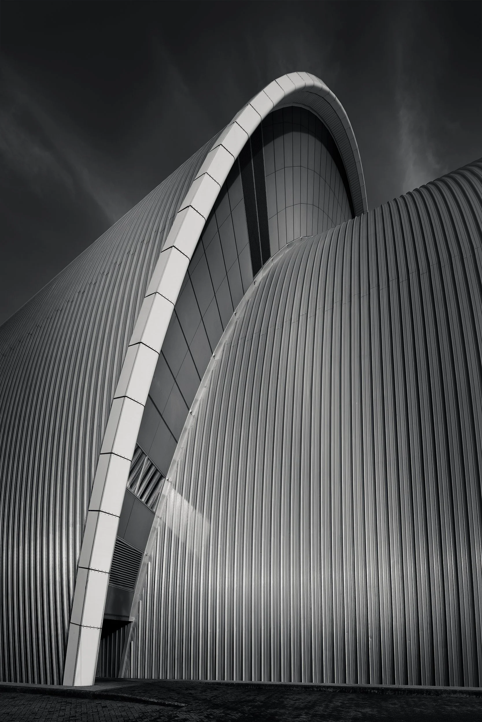 Neo-futurist architecture in Glasgow, Scotland: A dramatic monochromatic study of the SEC Armadillo (Clyde Auditorium), designed by Foster + Partners. This architectural photograph captures the rhythmic, overlapping aluminium "scales" and the sharp, 