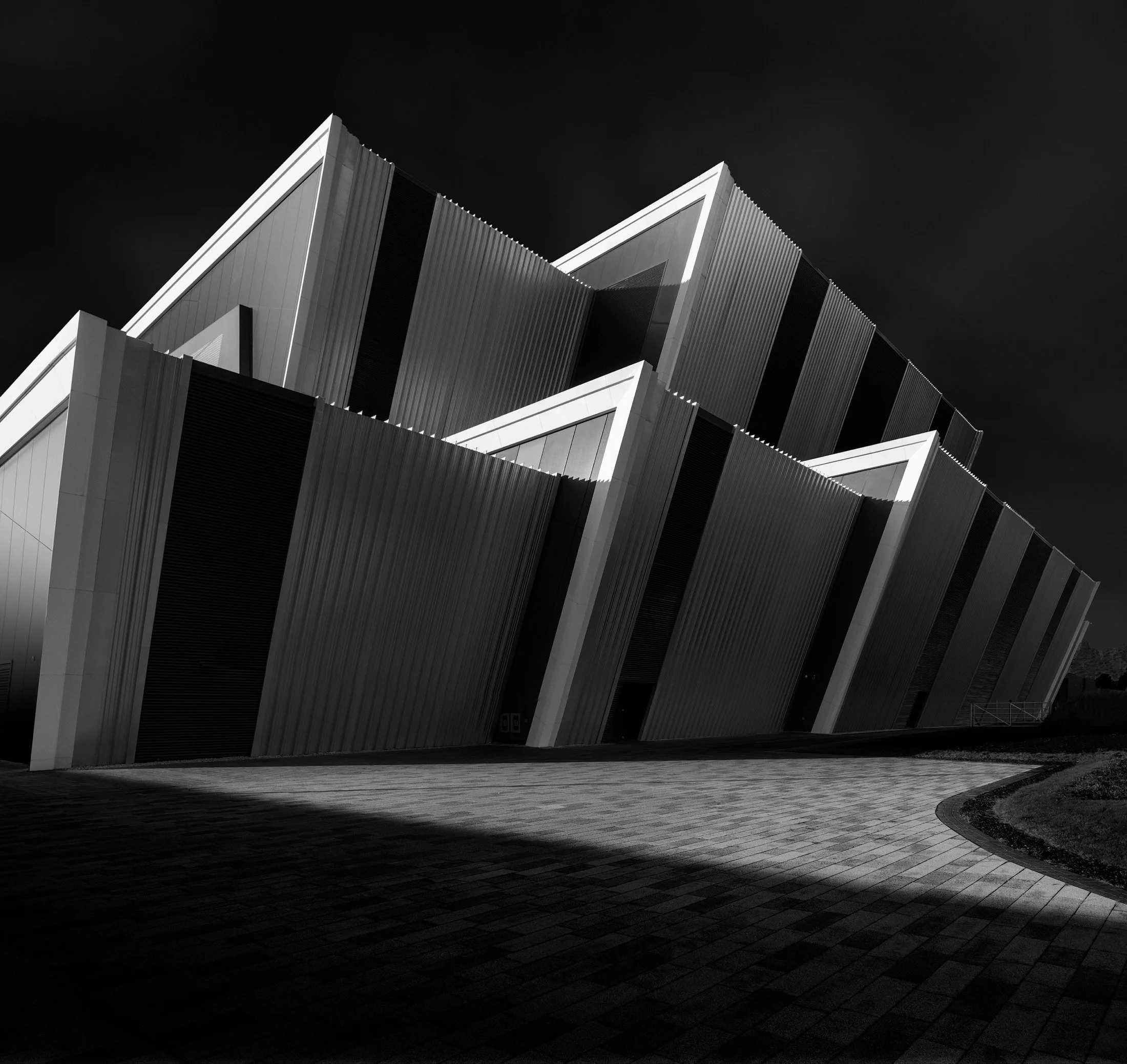 Contemporary event architecture in Aberdeen, Scotland: A dramatic monochromatic study of the P&J Live at TECA (The Event Complex Aberdeen), designed by Keppie Design. This low-angle architectural photograph captures the rhythmic, saw-tooth geometry o