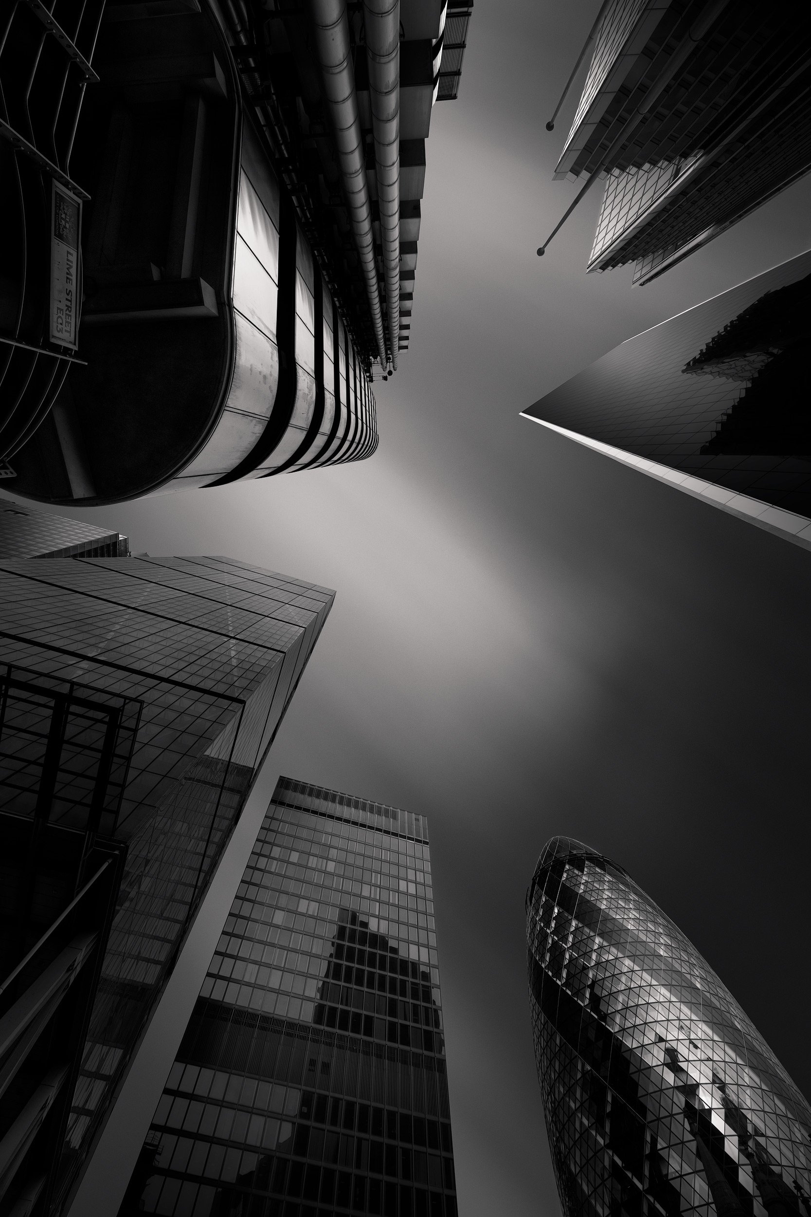 [architecture] [uk] [london] [blackandwhite] Upward through the City of London, Lloyd's of London, the Gherkin and Leadenhall converging against a moody grey sky. Architectural Photography by Jim Scott.