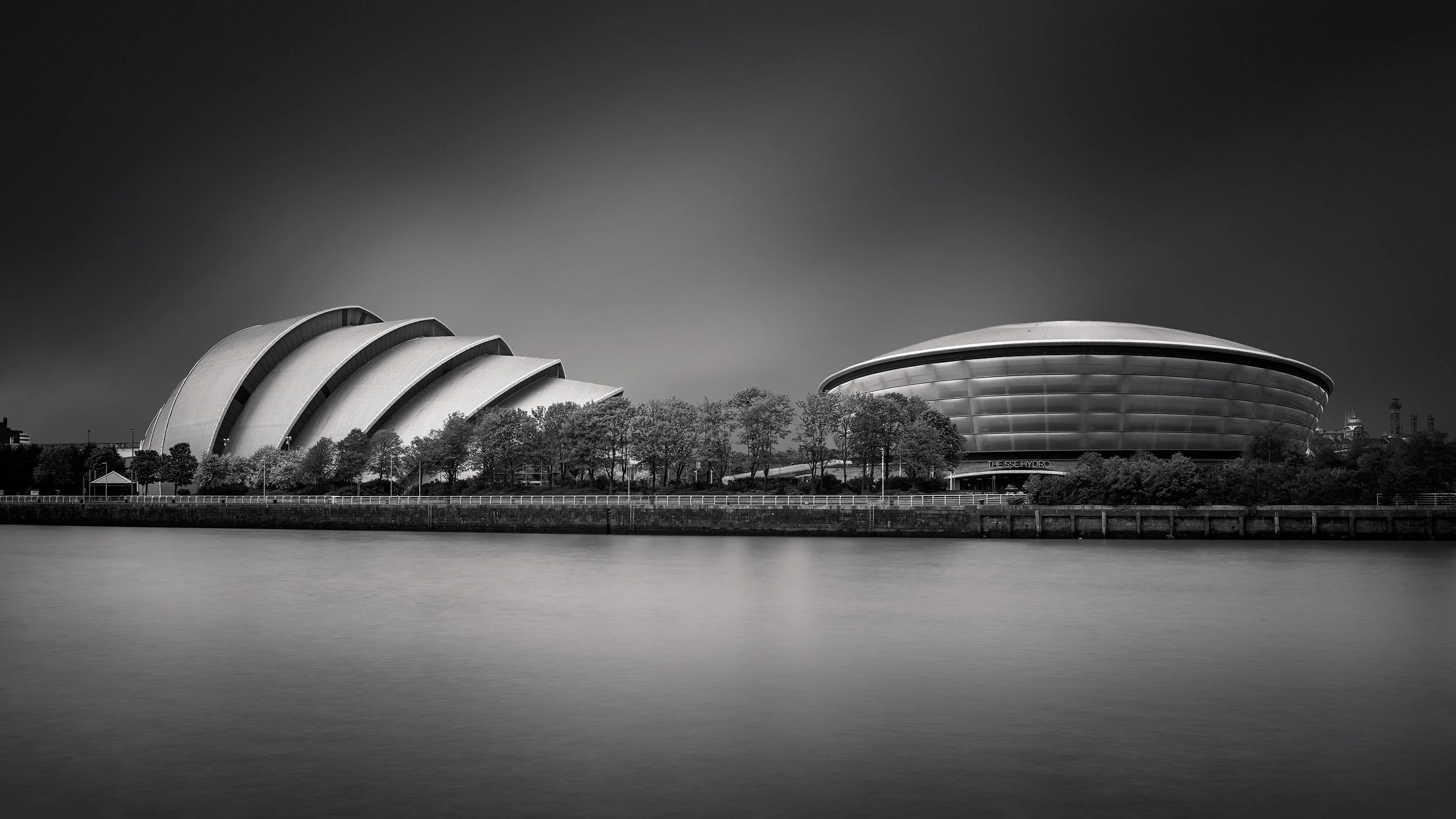 Contemporary architecture on the River Clyde, Glasgow: A panoramic study of the SEC Armadillo and the OVO Hydro arena, designed by Foster + Partners. This dramatic long-exposure photograph captures the contrasting geometries of the Armadillo’s interl