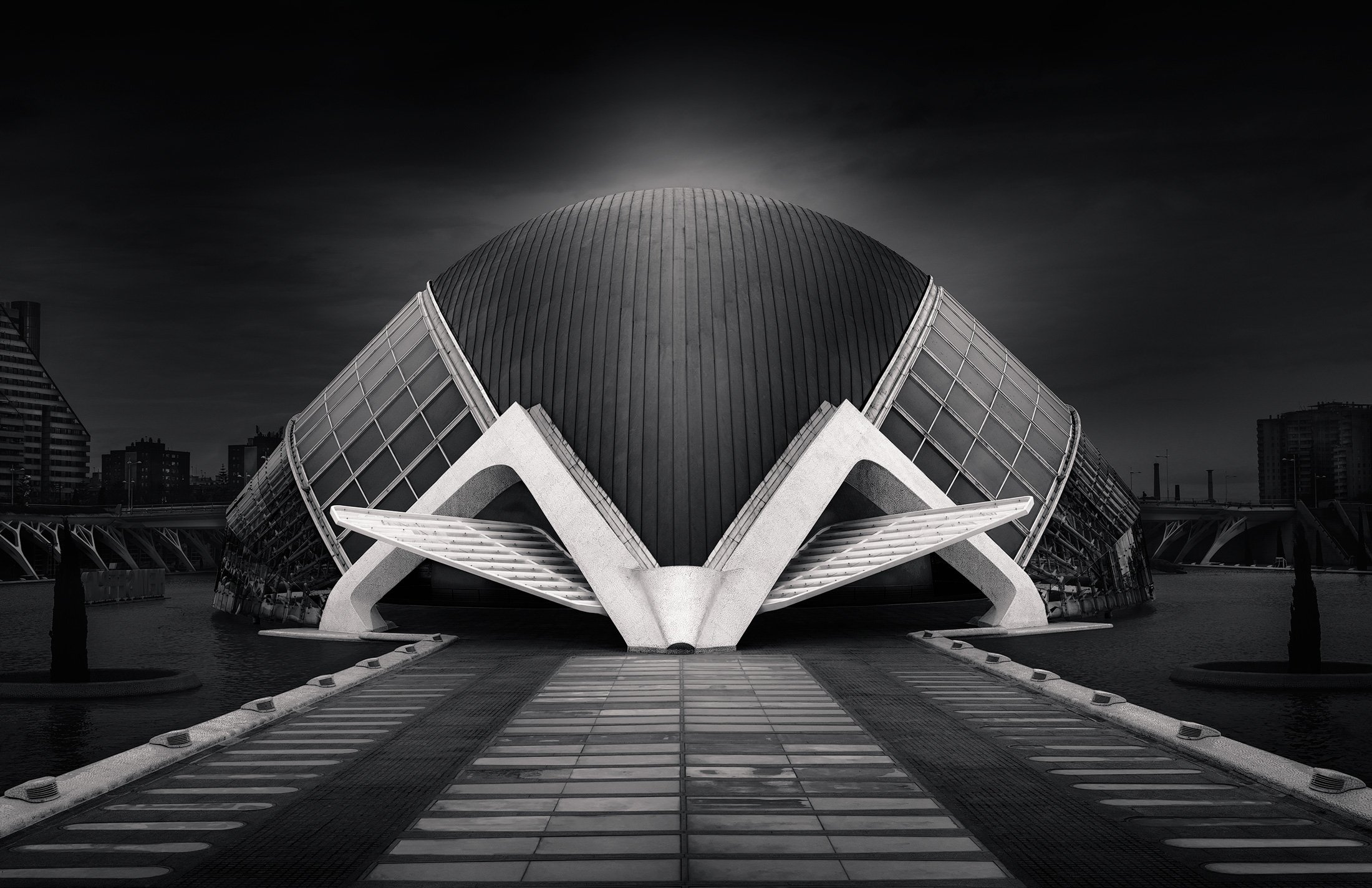 [architecture] [europe] [valencia] [blackandwhite] Hemisfèric Valencia B&W frontal, great dark ribbed dome flanked by two sweeping white concrete wing arches over water. Architectural Photography by Jim Scott.