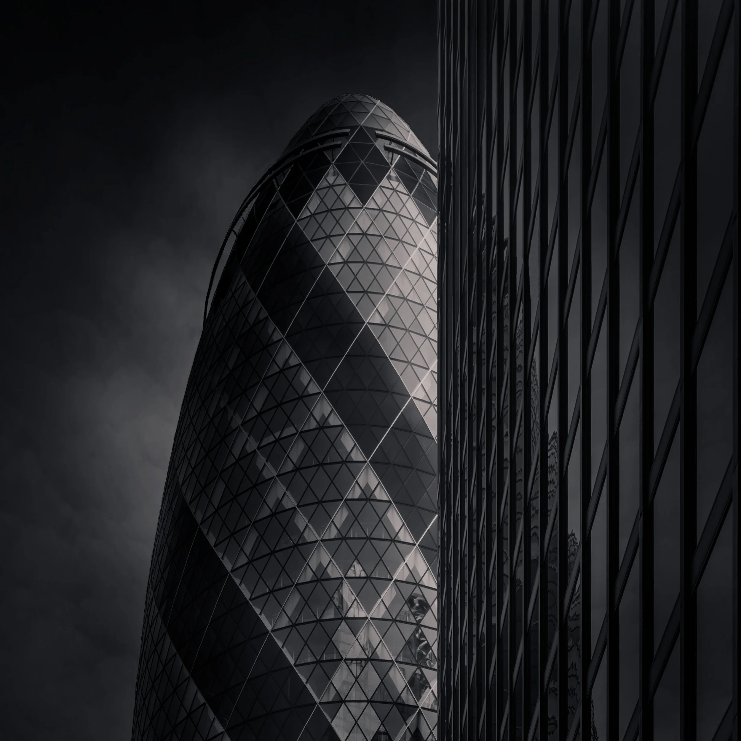 Iconic high-tech architecture in the City of London: A dramatic monochromatic study of 30 St Mary Axe (The Gherkin), designed by Foster + Partners. This architectural photograph uses a neighbouring glass facade to frame the building’s distinctive tap