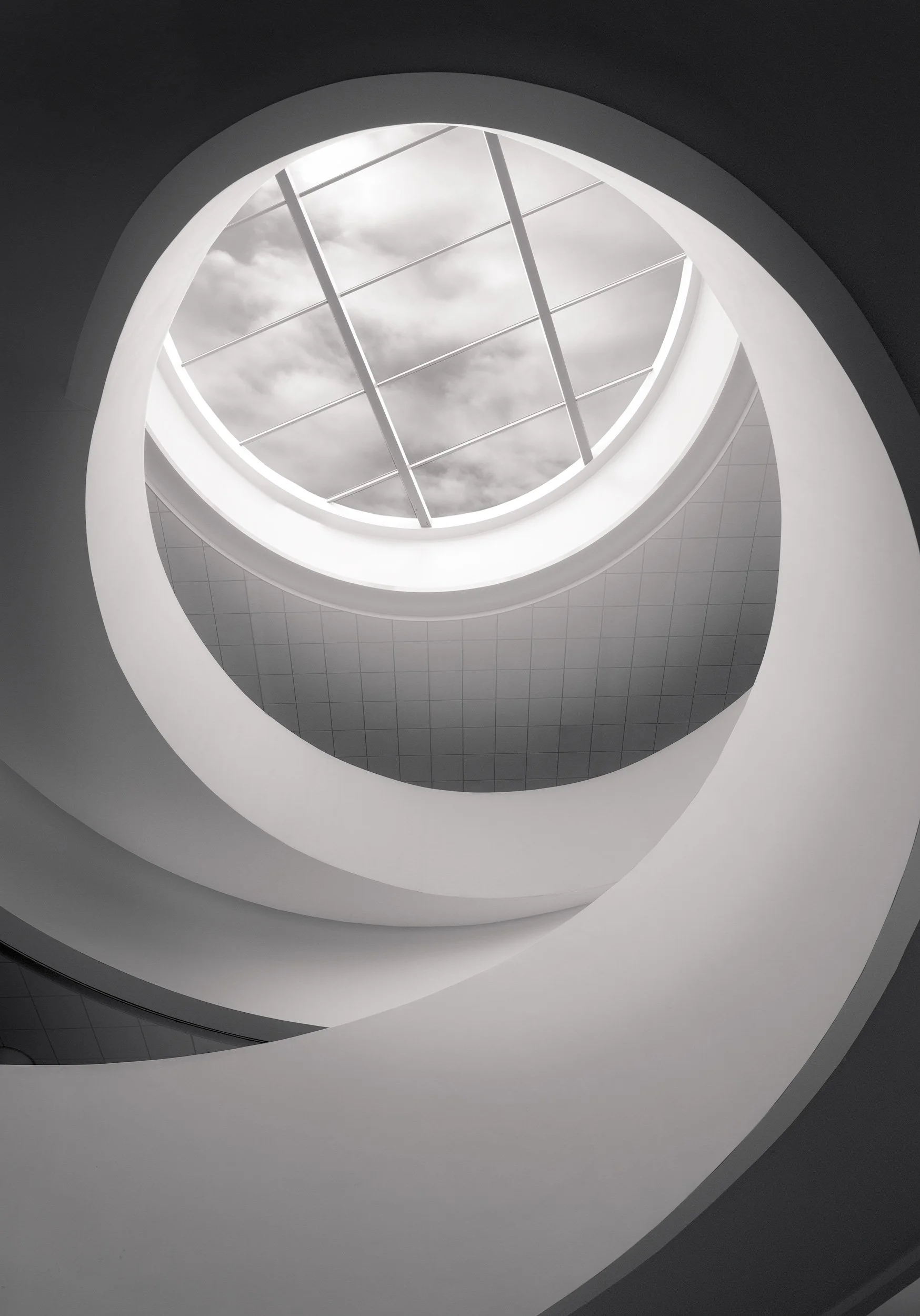 Contemporary architecture in Liverpool: The central spiral staircase of the Museum of Liverpool, designed by 3XN Architects. A stunning black and white vertical perspective showcasing the fluid, sculptural curves of the elliptical atrium and the bold
