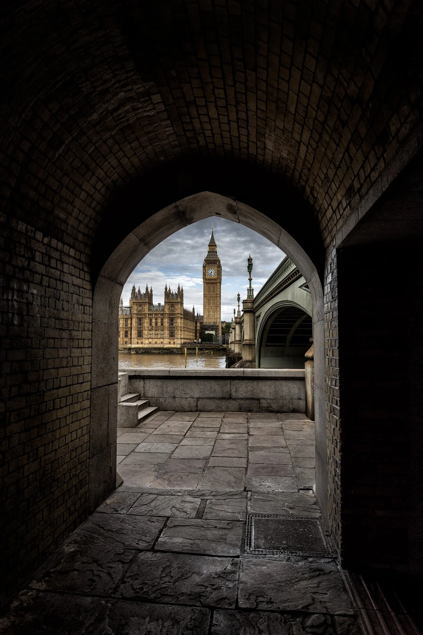 [architecture] [uk] [london] [colour] Big Ben and Houses of Parliament framed through a dark Gothic brick archway, Westminster Bridge visible beyond. Architectural Photography by Jim Scott.