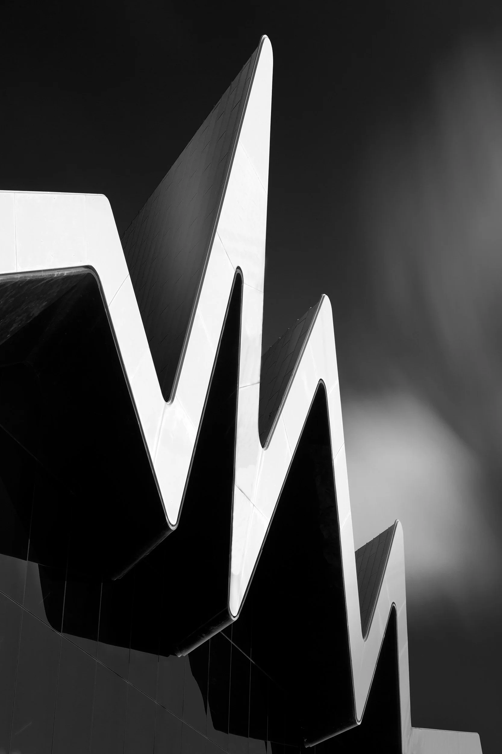 Contemporary waterfront architecture in Glasgow, Scotland: A dramatic abstract study of the Riverside Museum’s rhythmic, pleated roofline, designed by Zaha Hadid. This minimalist photograph isolates the sharp, zigzagging geometry of the zinc-clad str