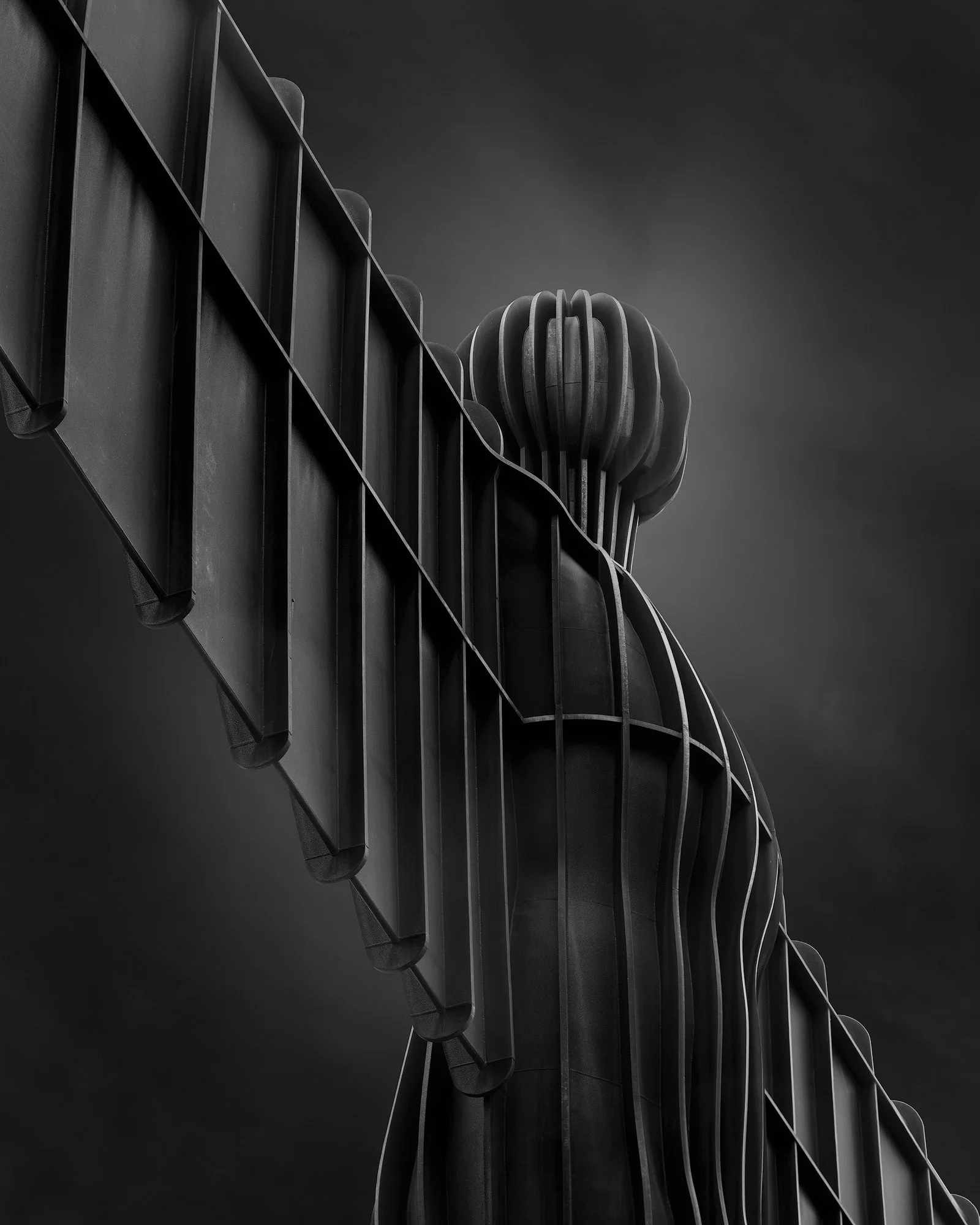 Contemporary public sculpture in Gateshead, UK: A minimalist monochromatic study of the Angel of the North, designed by Antony Gormley. This architectural photograph captures the rhythmic vertical ribs and the silhouette of the head and outstretched 