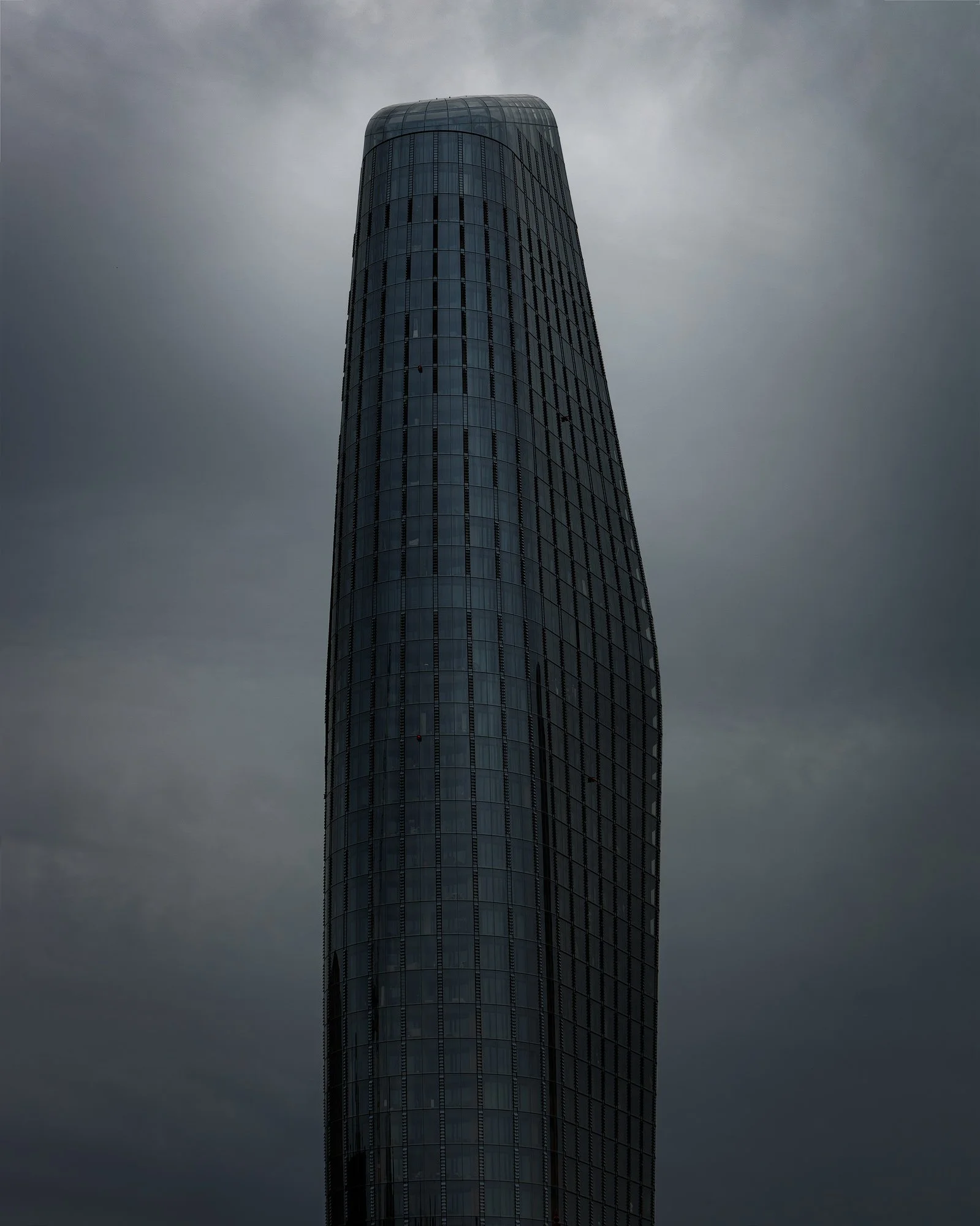 Modern residential architecture on London’s South Bank: A dramatic monochromatic study of One Blackfriars (The Vase), designed by SimpsonHaugh and Partners. This vertical architectural photograph captures the skyscraper’s iconic asymmetrical silhouet