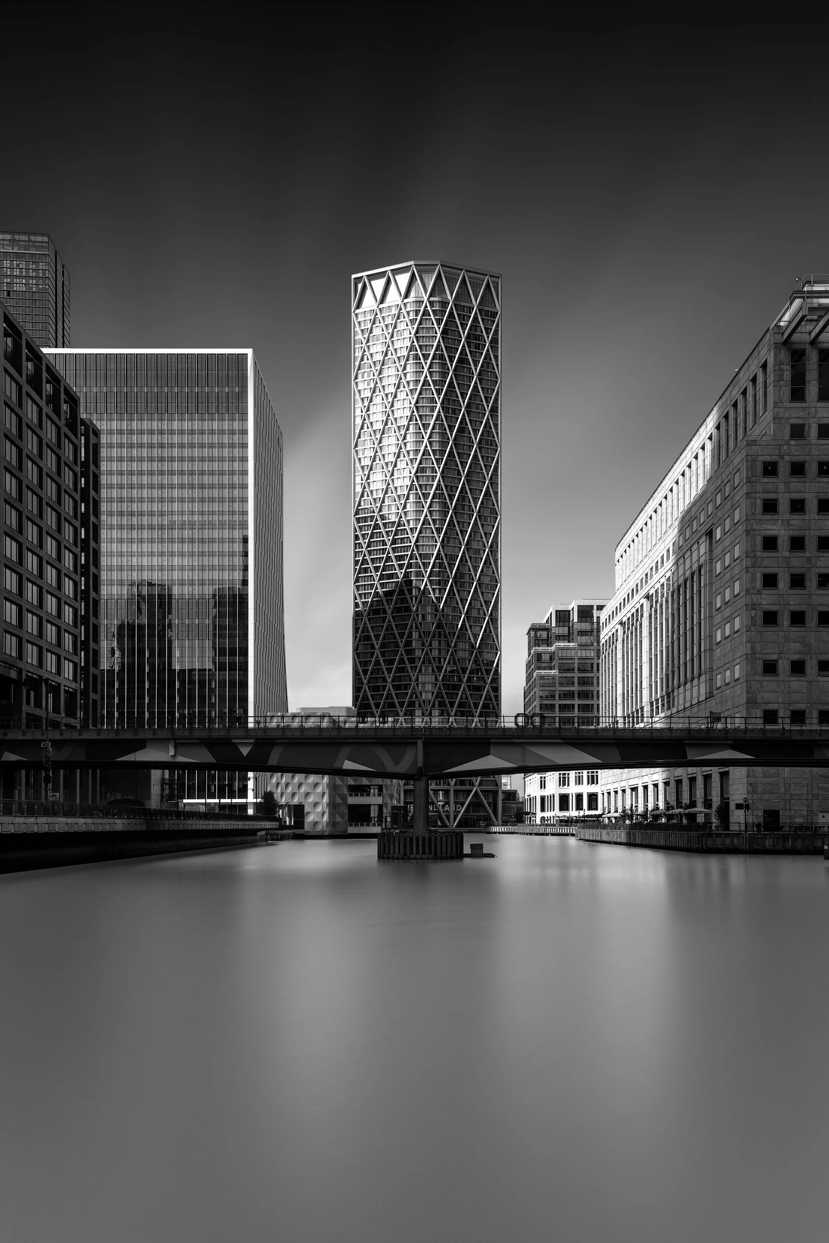 [architecture] [uk] [london] [blackandwhite] Newfoundland tower from Middle Dock monochrome, the diagrid cylinder centred above a silk-smooth dock and DLR bridge. Architectural Photography by Jim Scott.