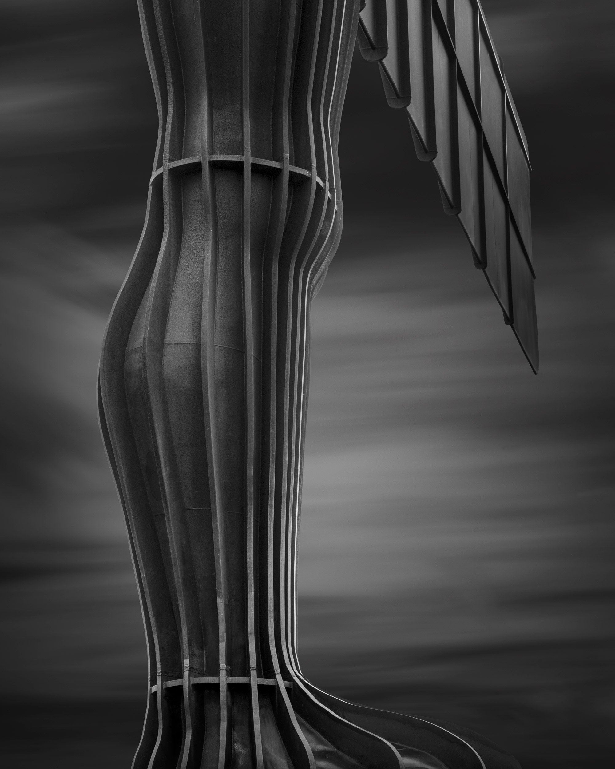 Contemporary public sculpture in Gateshead, UK: A minimalist monochromatic study of the Angel of the North, designed by Antony Gormley. This abstract architectural photograph captures the rhythmic vertical ribs and weathered weathering-steel texture 