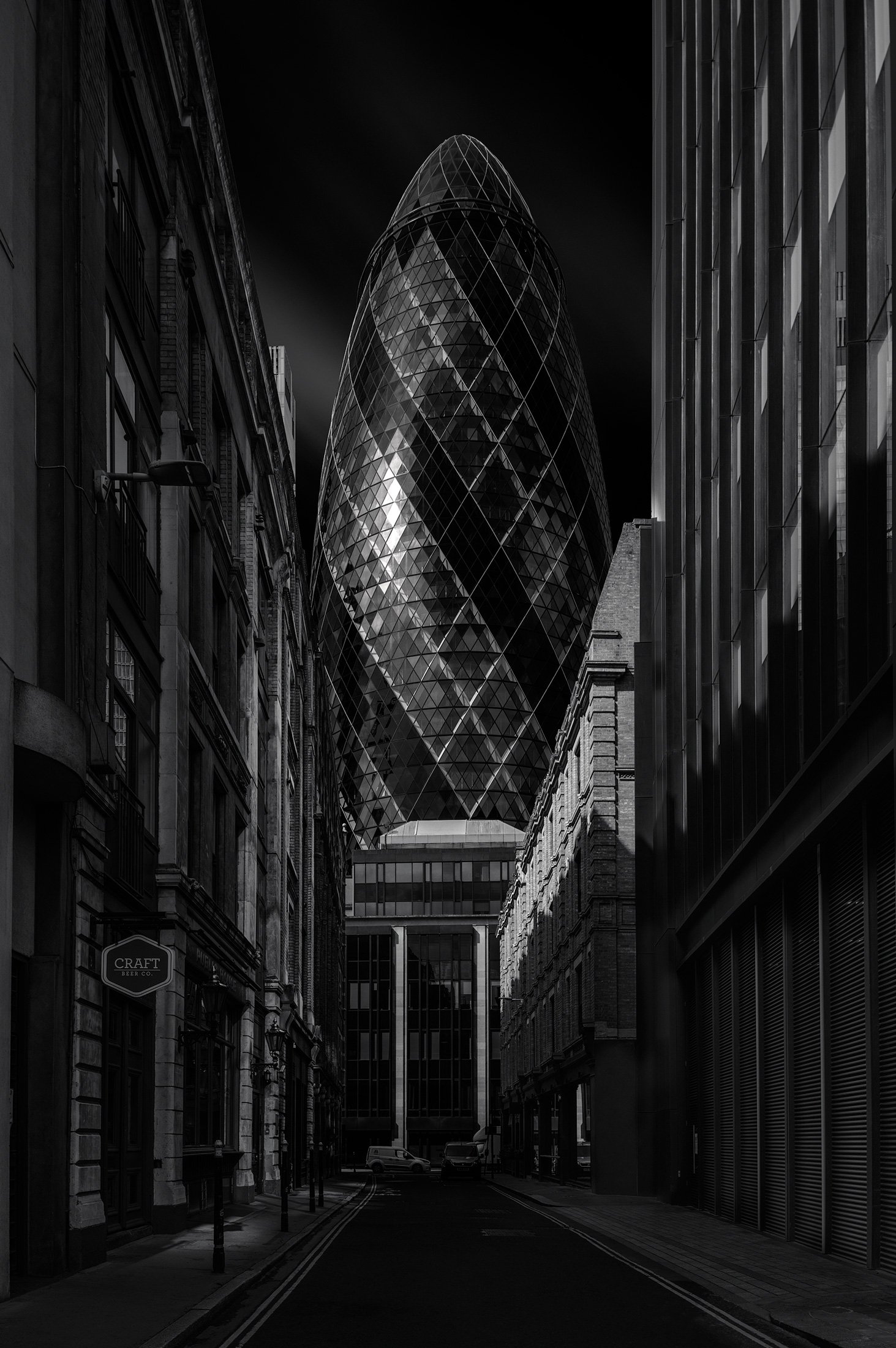 Iconic high-tech architecture in the City of London: A dramatic monochromatic study of 30 St Mary Axe (The Gherkin) viewed from Mitre Street, designed by Foster + Partners. This architectural photograph captures the building’s spiralling diagrid faca