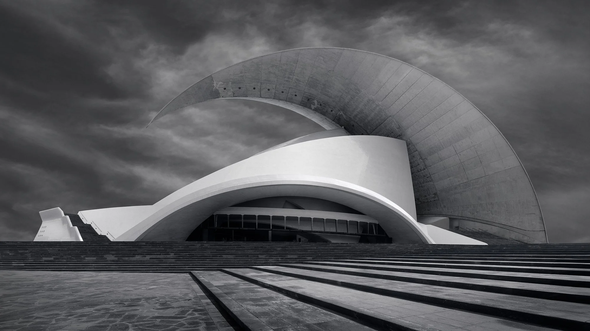 [architecture] [europe] [santacruzdetenerife] [blackandwhite] [panoramic] Auditorio de Tenerife Santa Cruz, Calatrava's sweeping concrete crescent arch and layered white shell forms above plaza. Architectural Photography by Jim Scott.