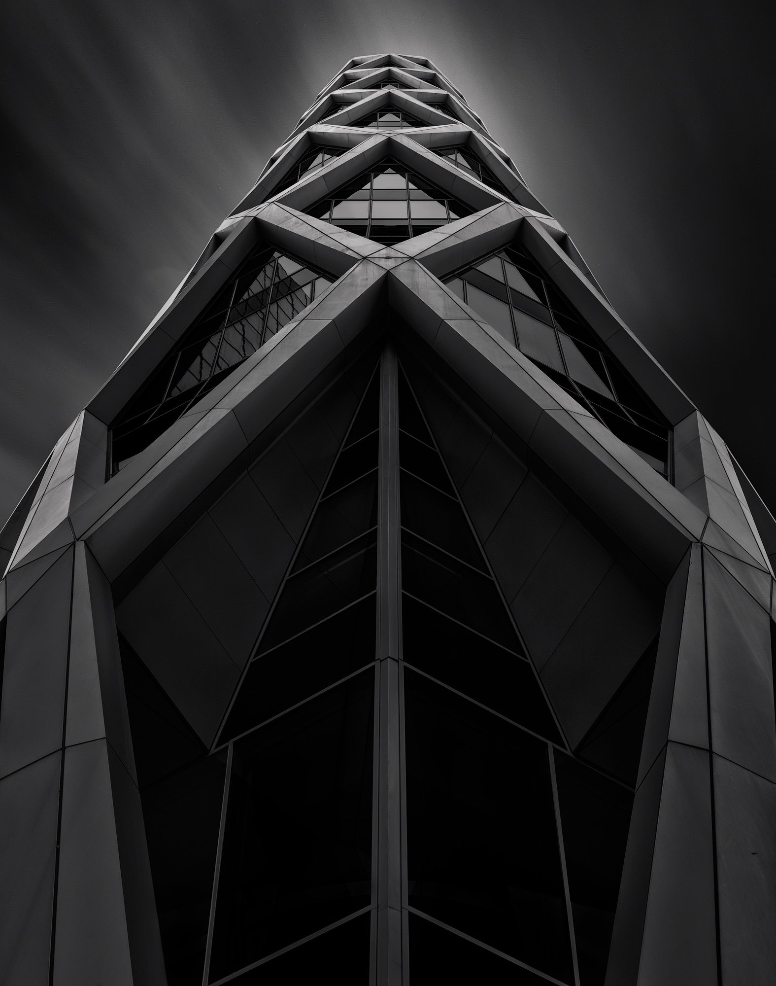 A tall modern building with a geometric, angular facade taken from ground level looking up, in black and white.