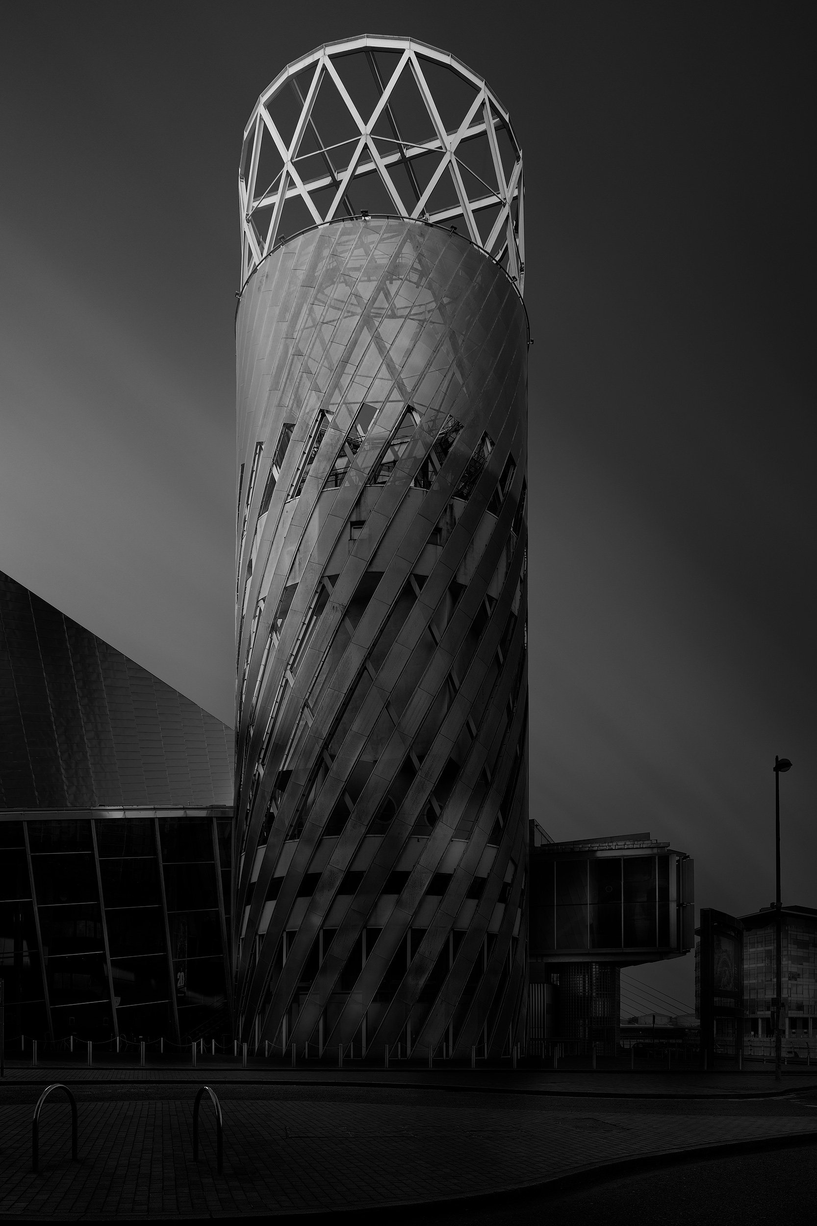 [architecture] [uk] [salford] [blackandwhite] Lowry Theatre tower at MediaCityUK Salford, spiralling glazed cylinder with white diagrid crown against a dark sky. Architectural Photography by Jim Scott.