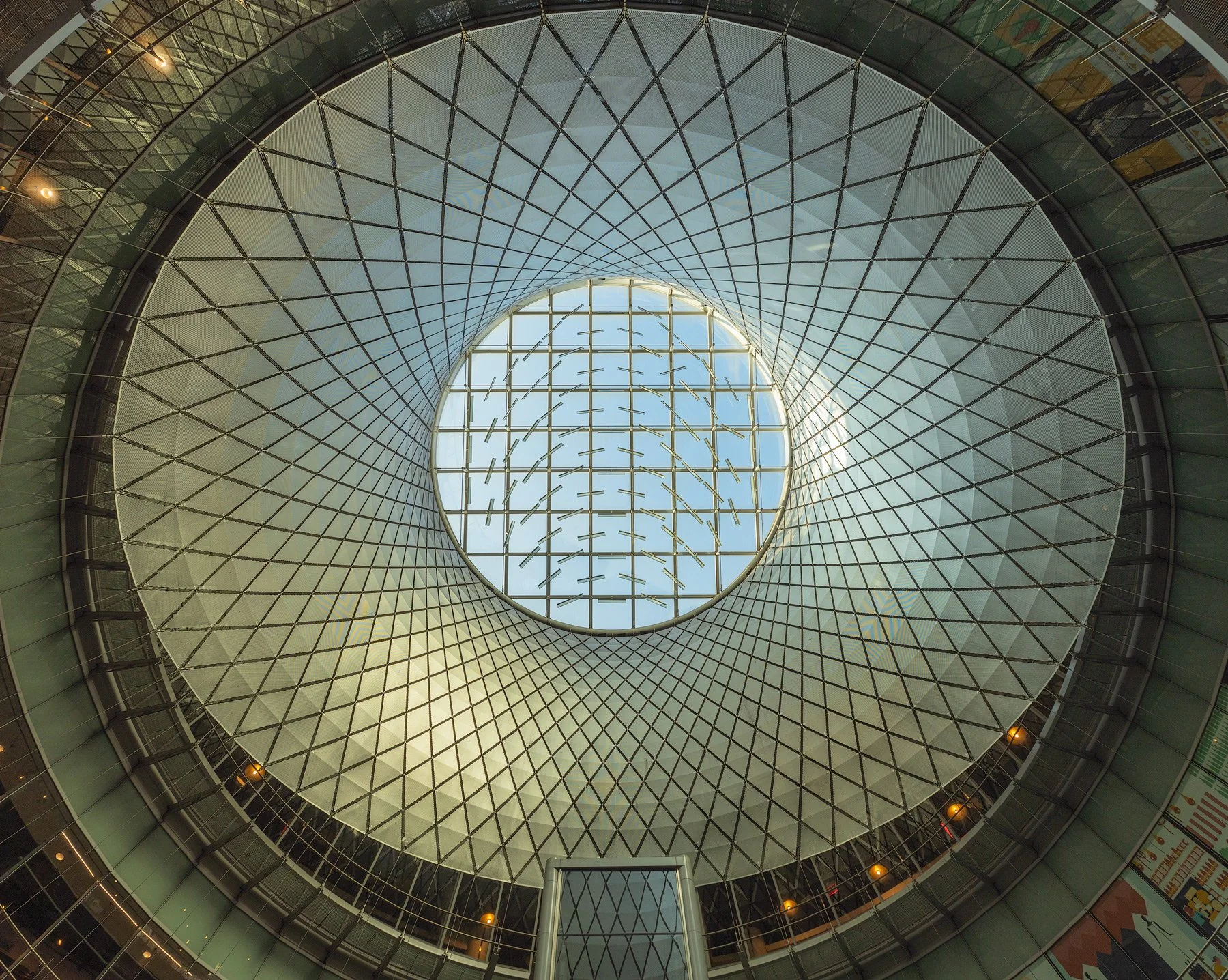 High-tech transit architecture in Lower Manhattan, NYC: A symmetrical interior study of the Fulton Center’s Sky Reflector-Net, designed by Grimshaw Architects and Arup. This photograph captures the intricate geometry of the light-reflecting cable net