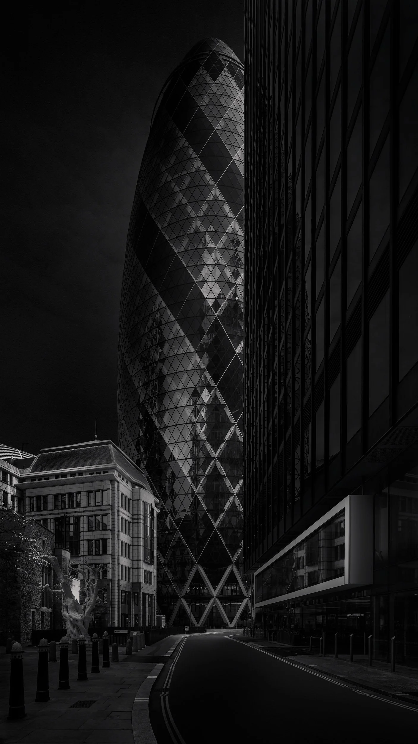 [architecture] [uk] [london] [blackandwhite] 30 St Mary Axe Gherkin London, street level view between City buildings with sculpture and empty road, dark dramatic scene. Architectural Photography by Jim Scott.
