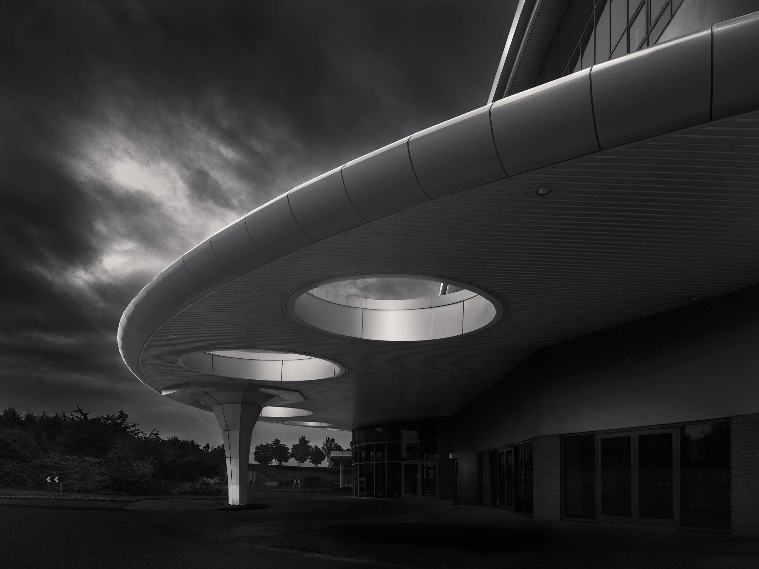 [architecture] [uk] [aberdeen] [blackandwhite] King's Community Church Aberdeen, with sweeping aluminium canopy and circular oculi on tapered columns under a dark sky. Architectural Photography by Jim Scott.